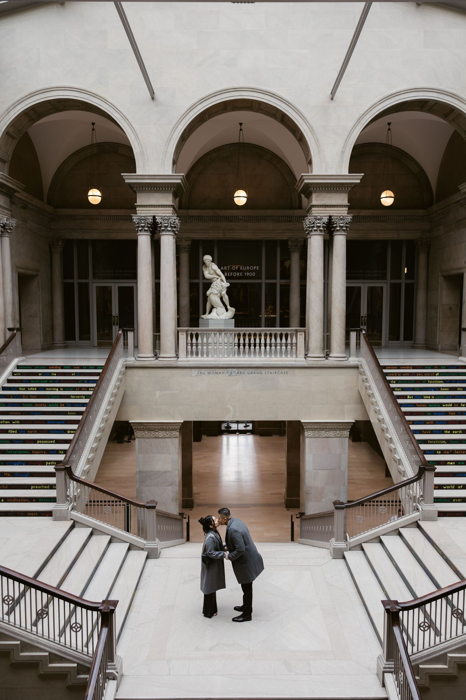 Classical museum interior with symmetrical arched colonnade and grand marble staircase.