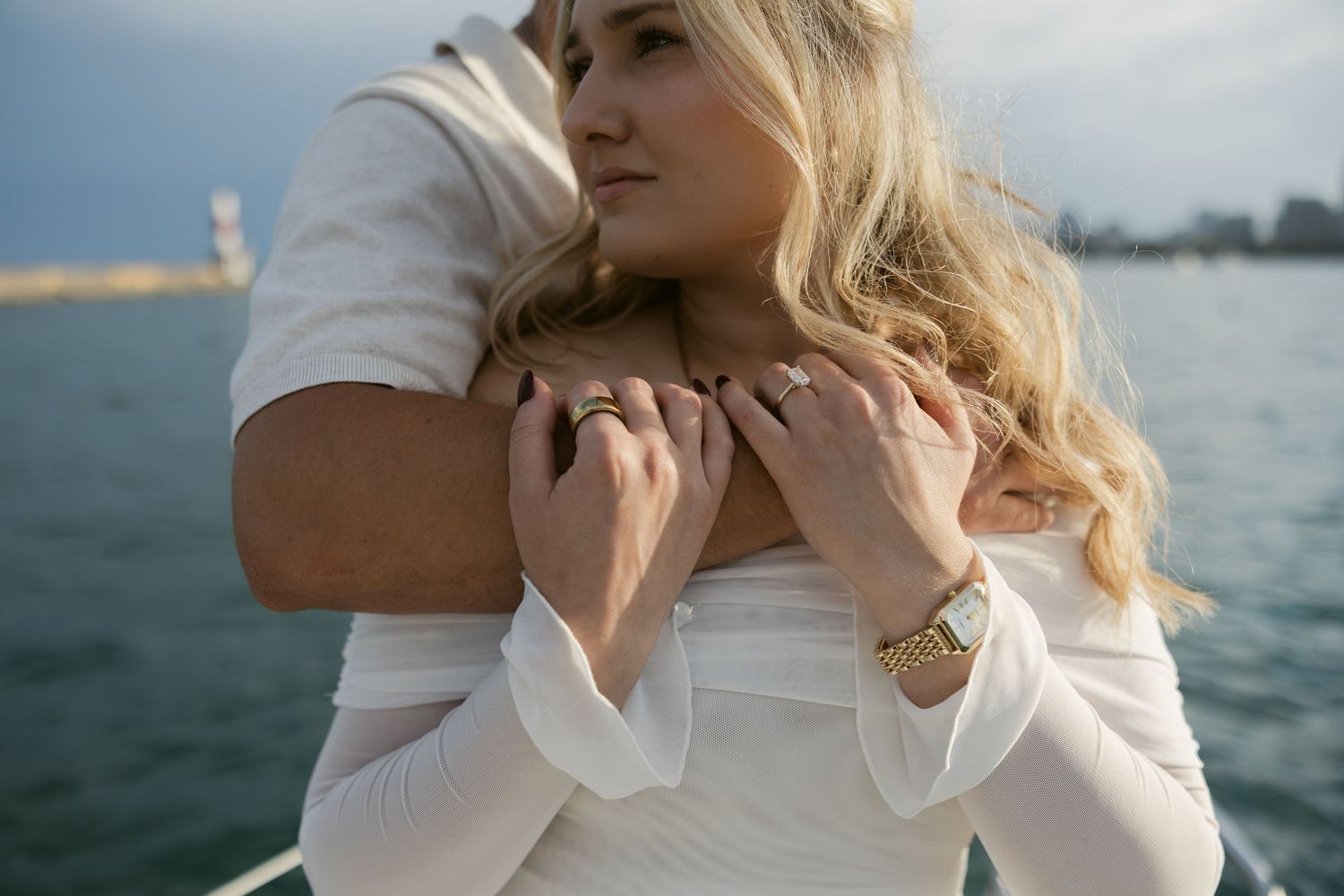 Close-up of blonde bride in white dress posing near water with blurred mountains and ocean in background.