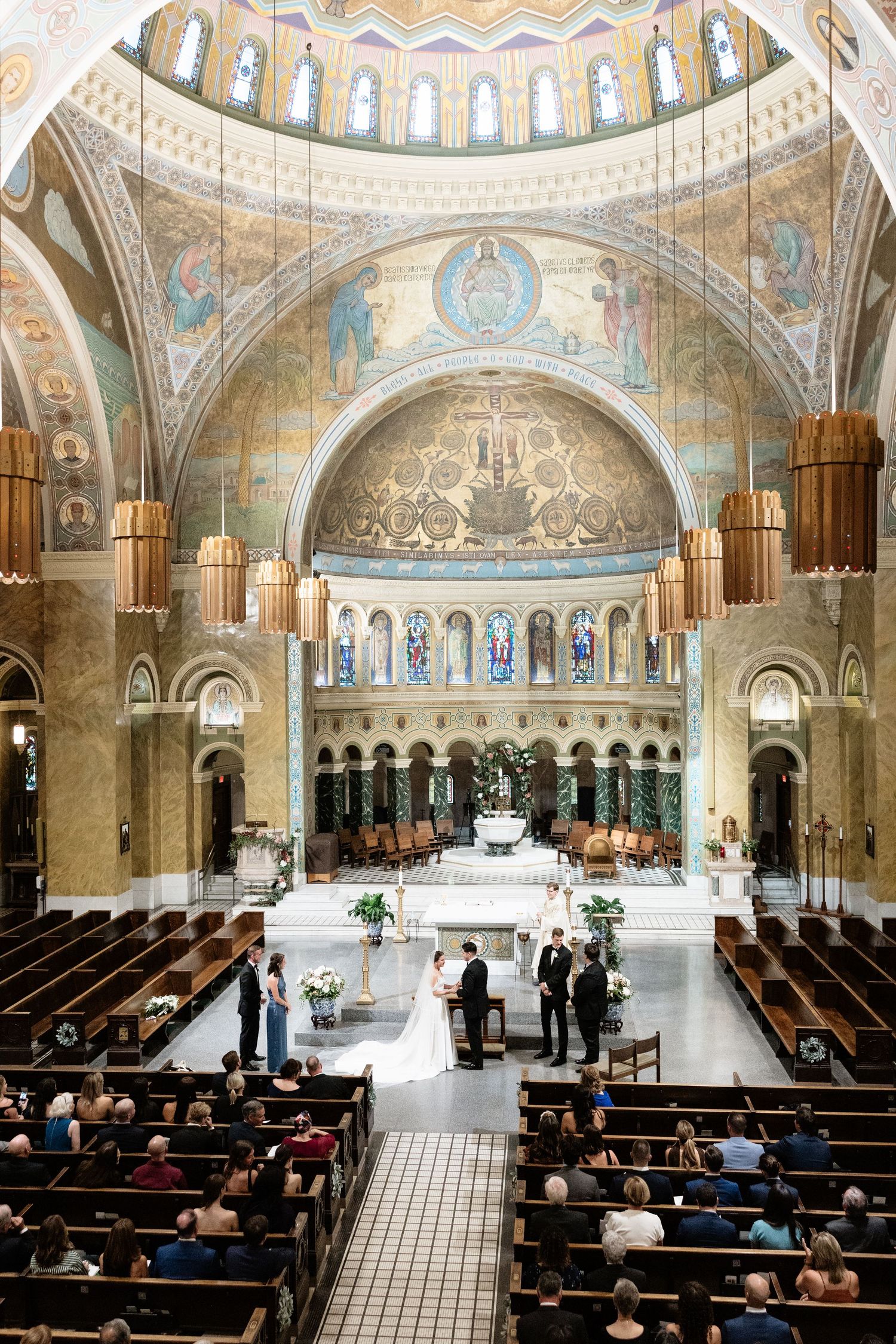Interior view of an ornate church sanctuary with domed ceiling, mosaic artwork, and rows of wooden pews.