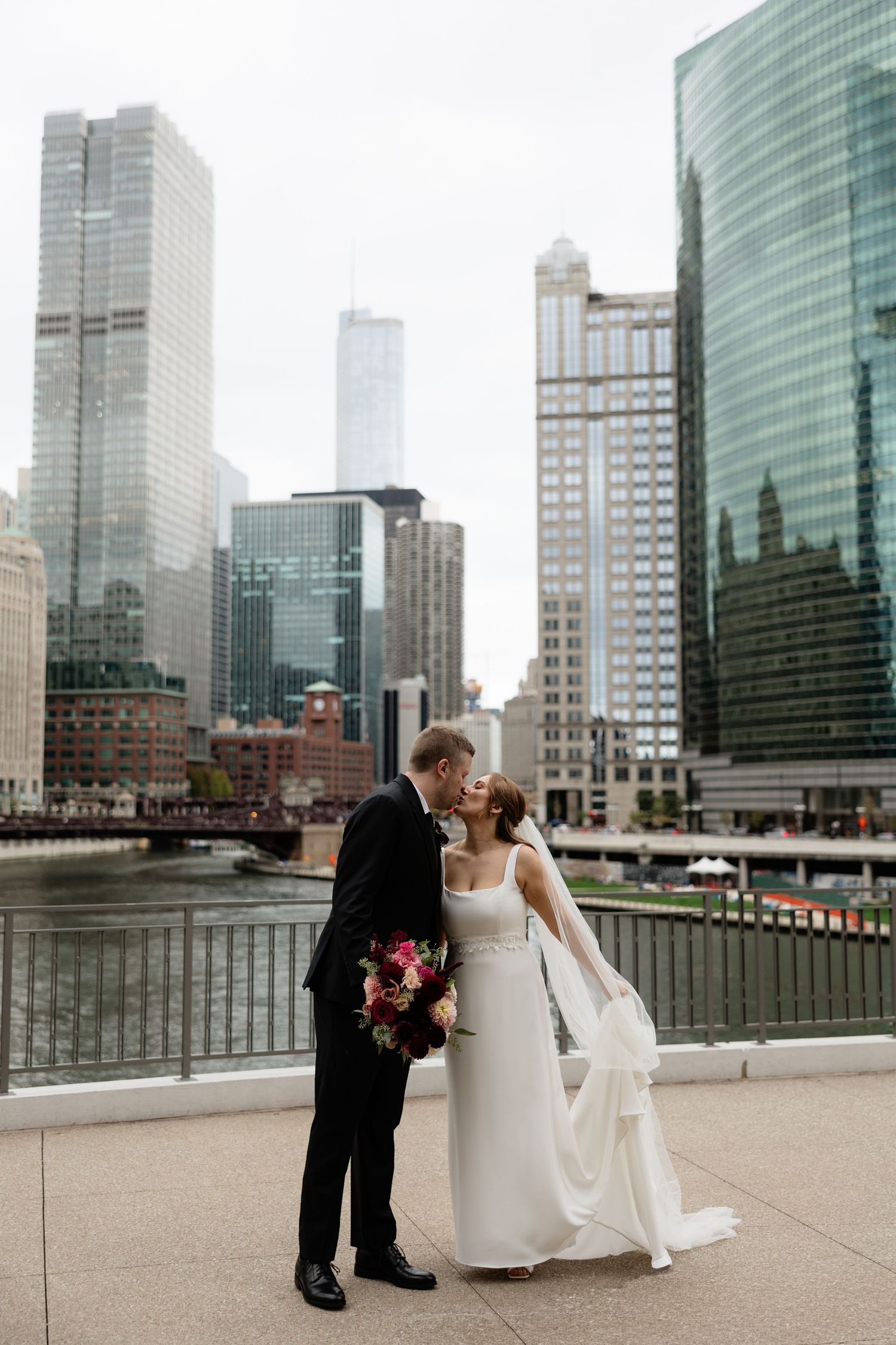 A wedding couple poses for romantic photos along the waterfront with modern city skyscrapers in the background.