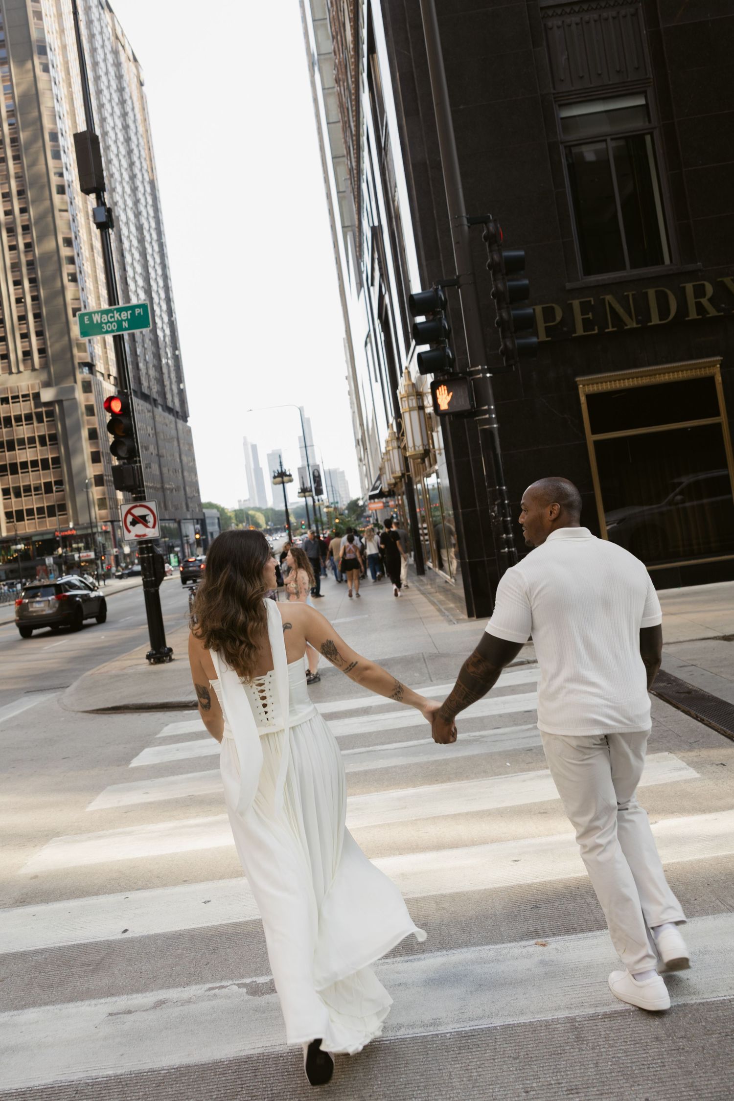 Couple in white outfits holding hands while running through downtown Chicago streets.