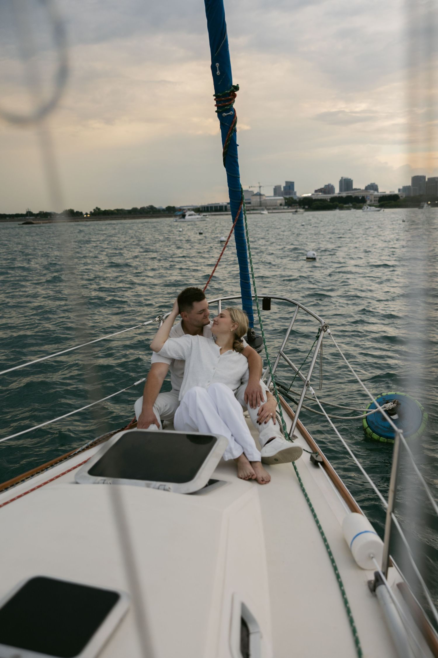 Romantic moment captured on a sailboat deck with water and cityscape views in the background.