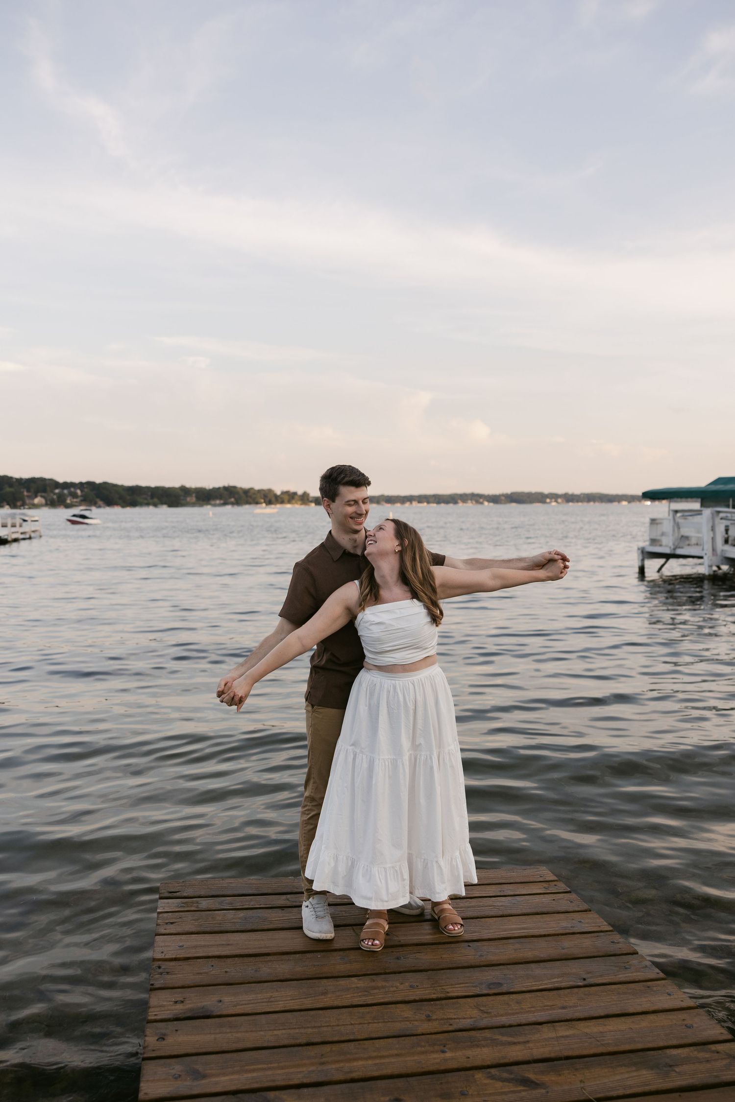 Couple in coordinated outfits posing playfully on wooden pier over lake.
