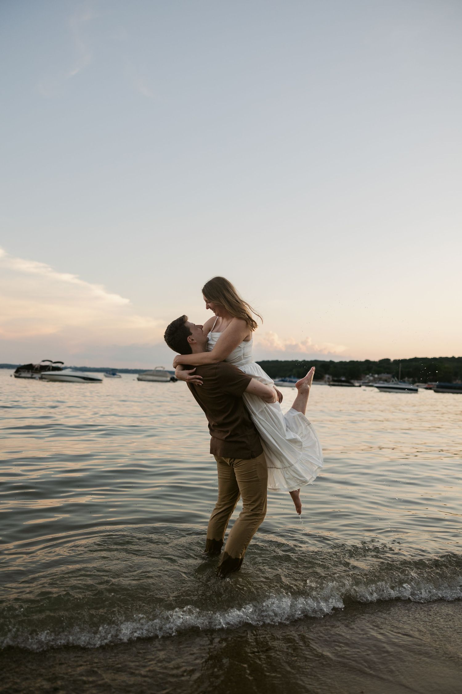 Couple dancing and splashing in shallow water during sunset at a lakeside beach.