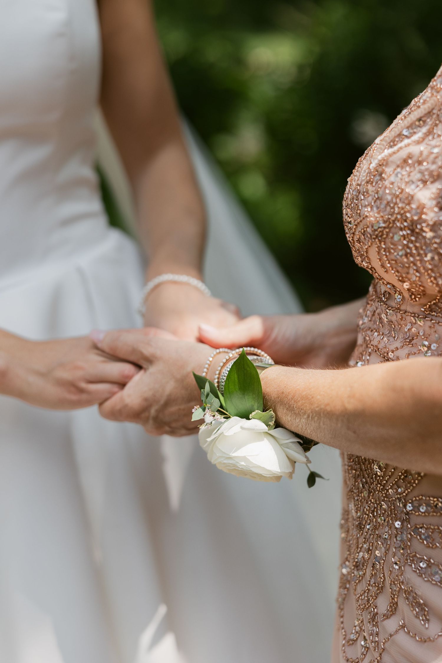 Close-up of a delicate white floral wrist corsage being adjusted during a wedding ceremony.