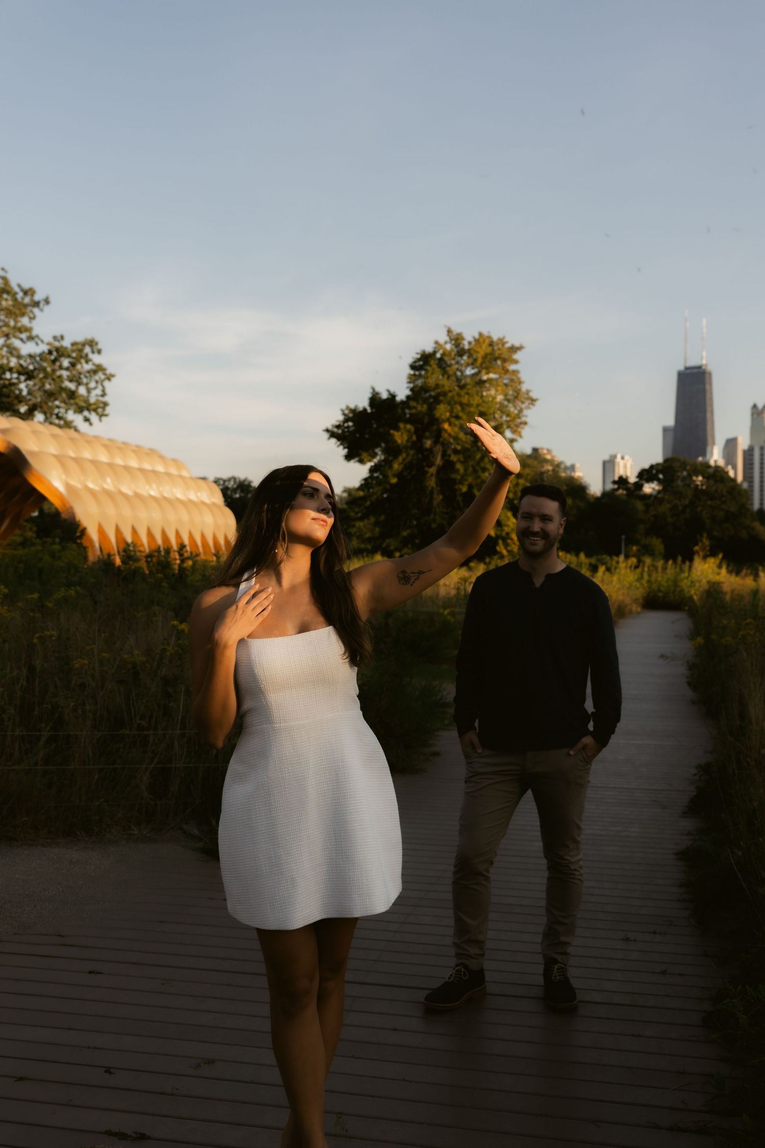 A couple laughs together on a deck with the city skyline visible in the background.