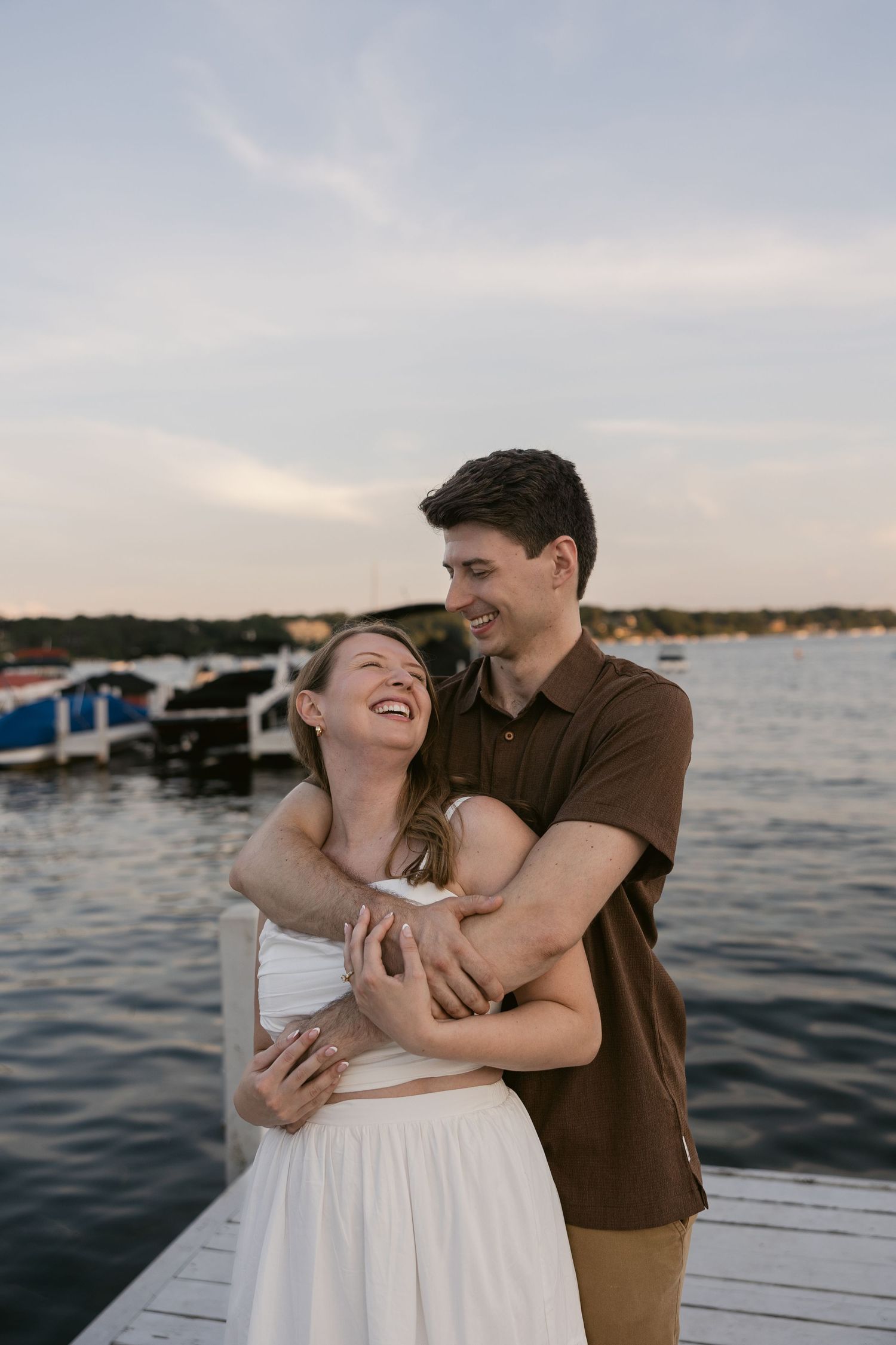 A joyful couple laughs together during their casual waterfront photo session at sunset.