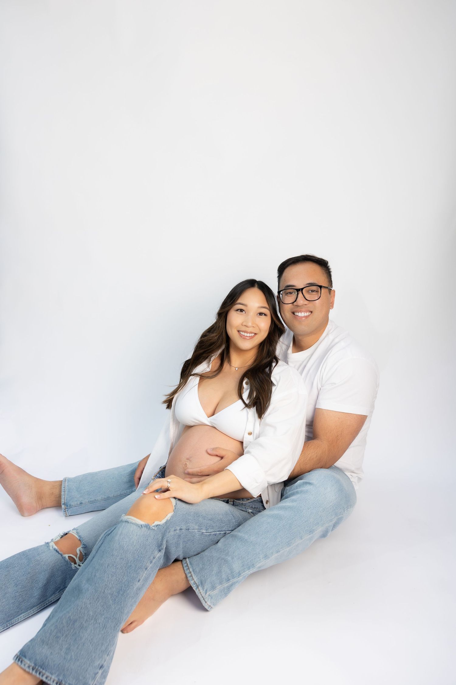 Couple in relaxed pose during maternity photoshoot on white background.