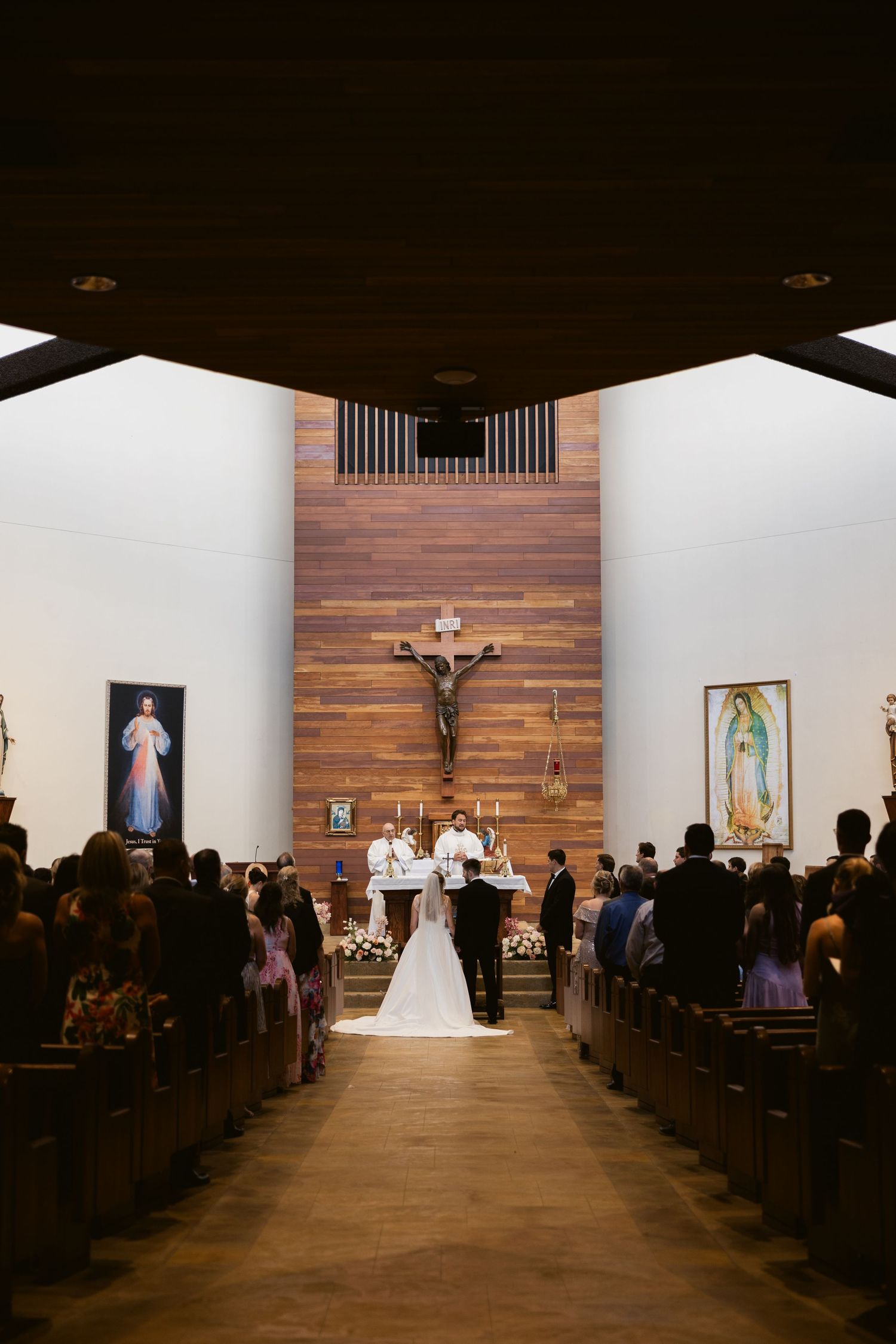 Wedding ceremony in a Catholic church with wooden walls and religious artwork.