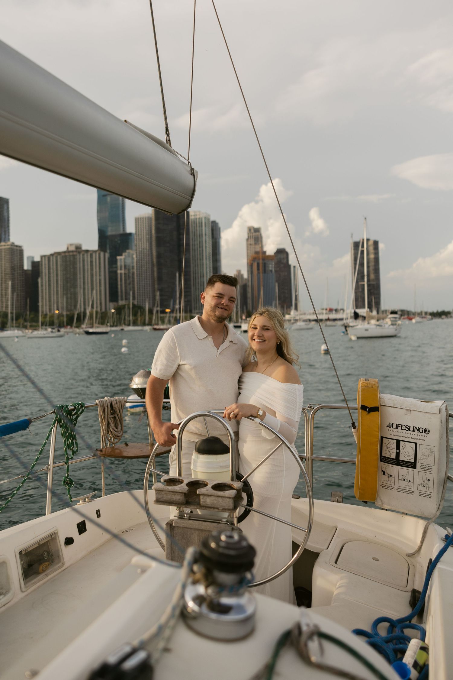 A couple standing at the helm of a sailboat with Chicago's magnificent skyline visible across the harbor.
