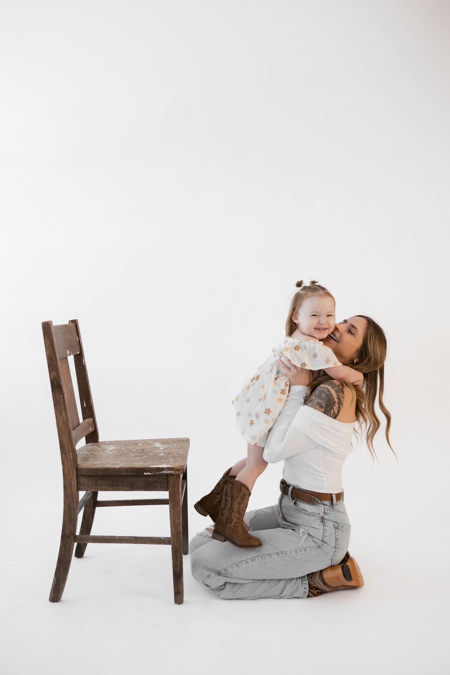 Loving interaction between adult and child next to wooden chair against white backdrop.