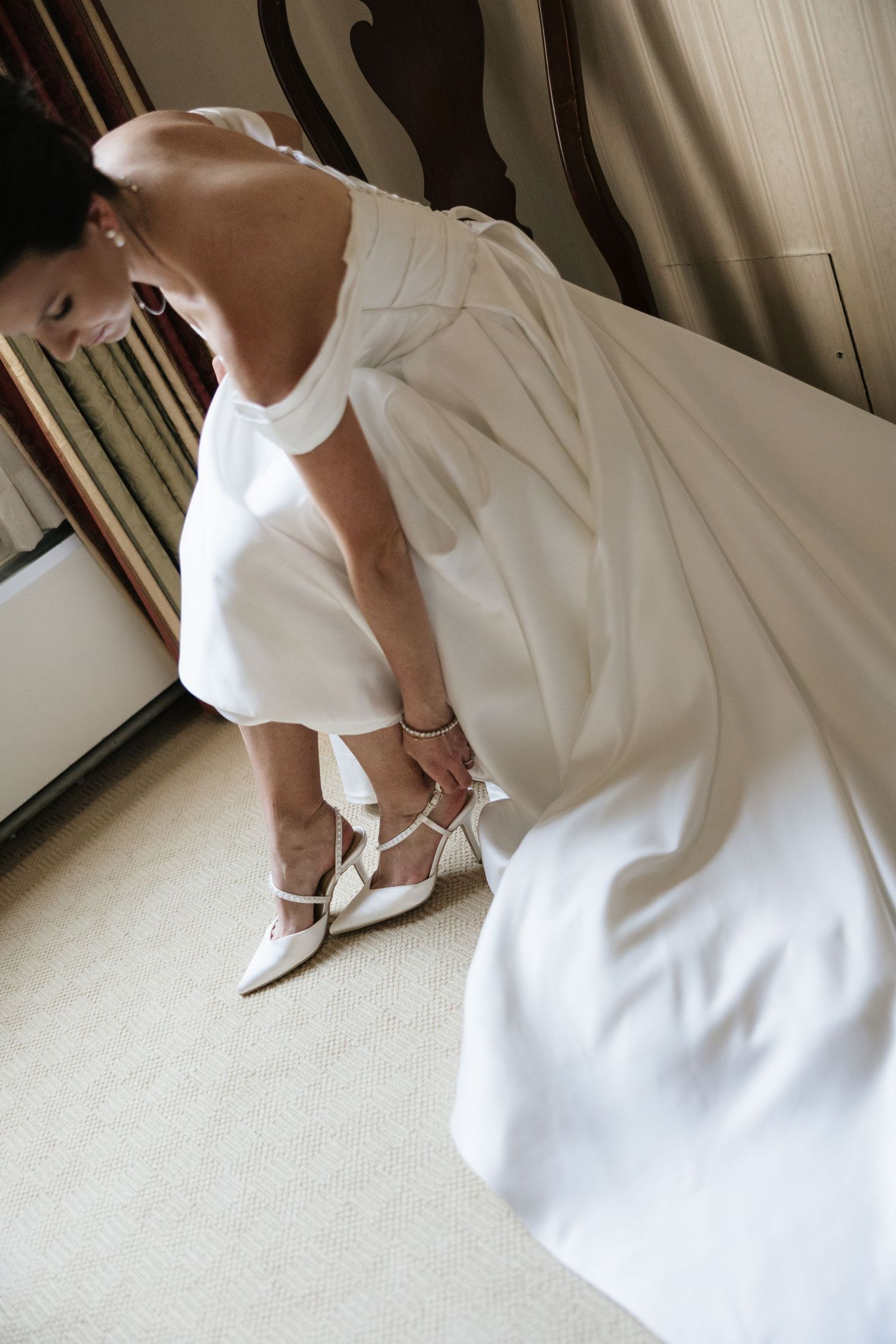 A series of photos showing details of an elegant white wedding dress and matching heels on a carpeted floor.