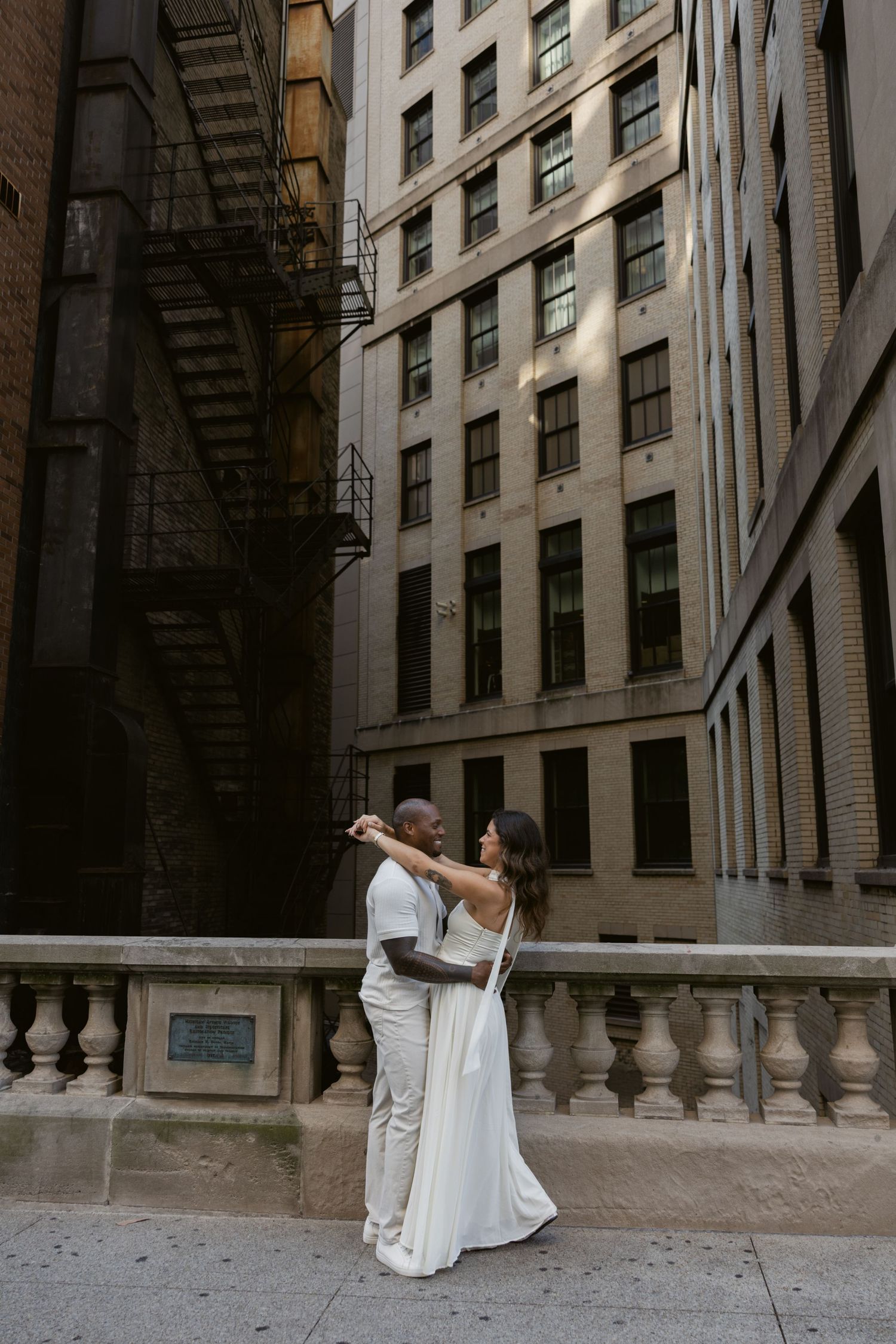 Couple in white outfits posing on exterior stairs of classic building in artistic dance-like poses.