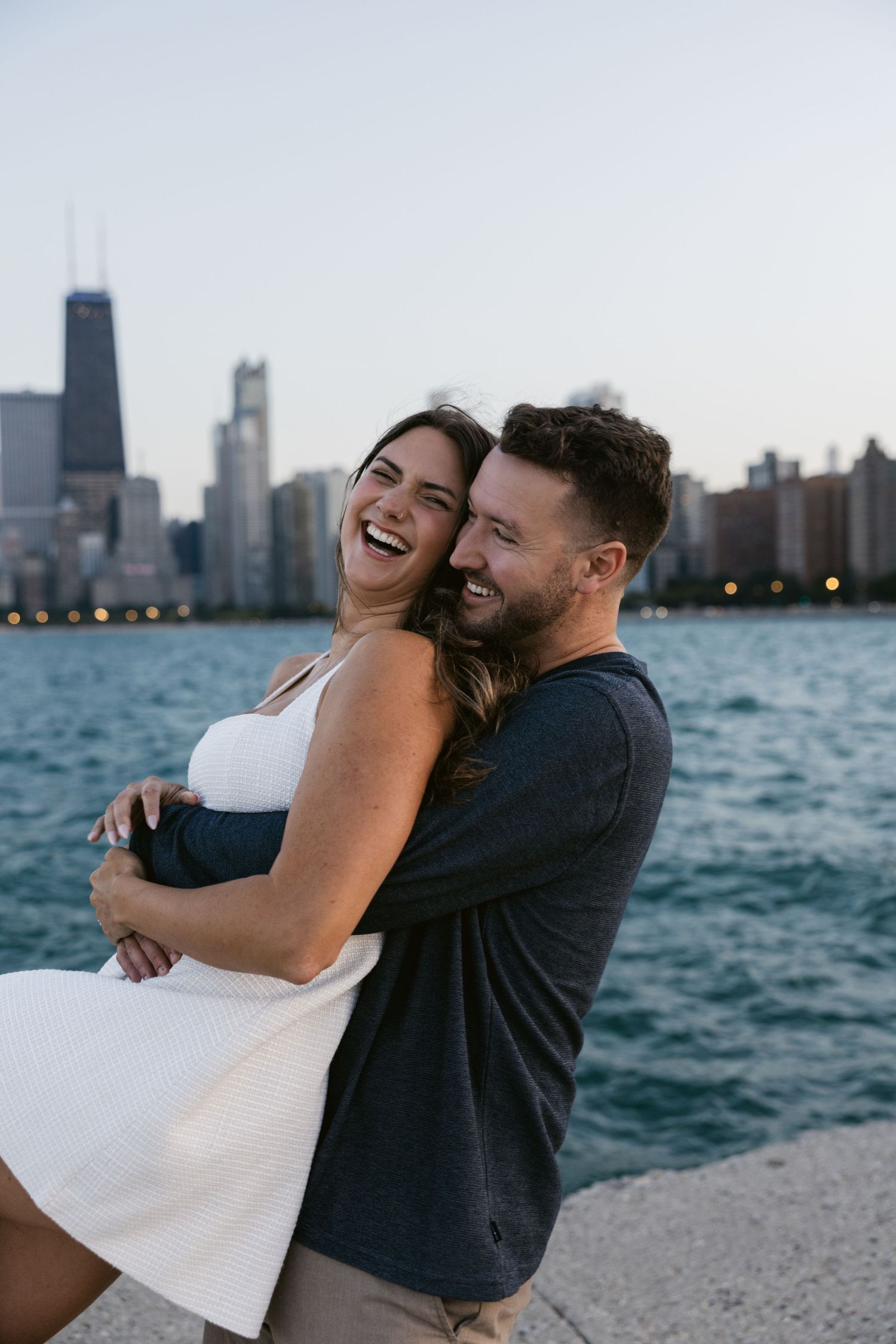 A joyful couple laughs together along Lake Michigan with Chicago's iconic skyscrapers in the distance.
