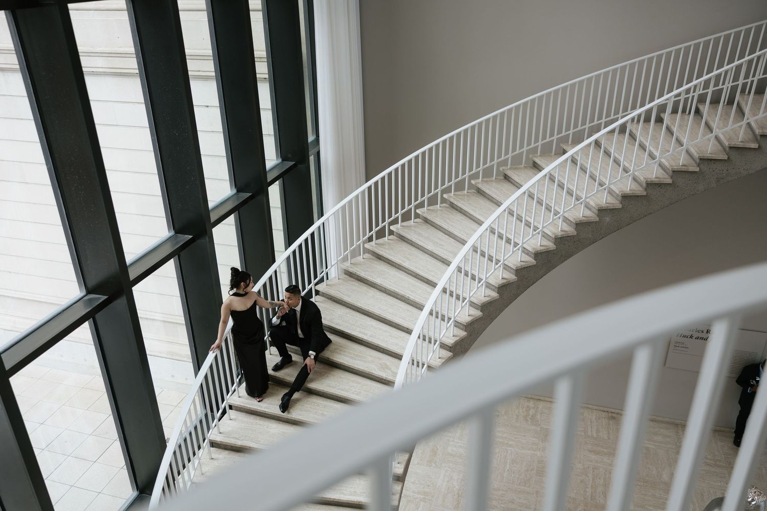 An elegant staircase with white railings curves upward in a modern building interior.