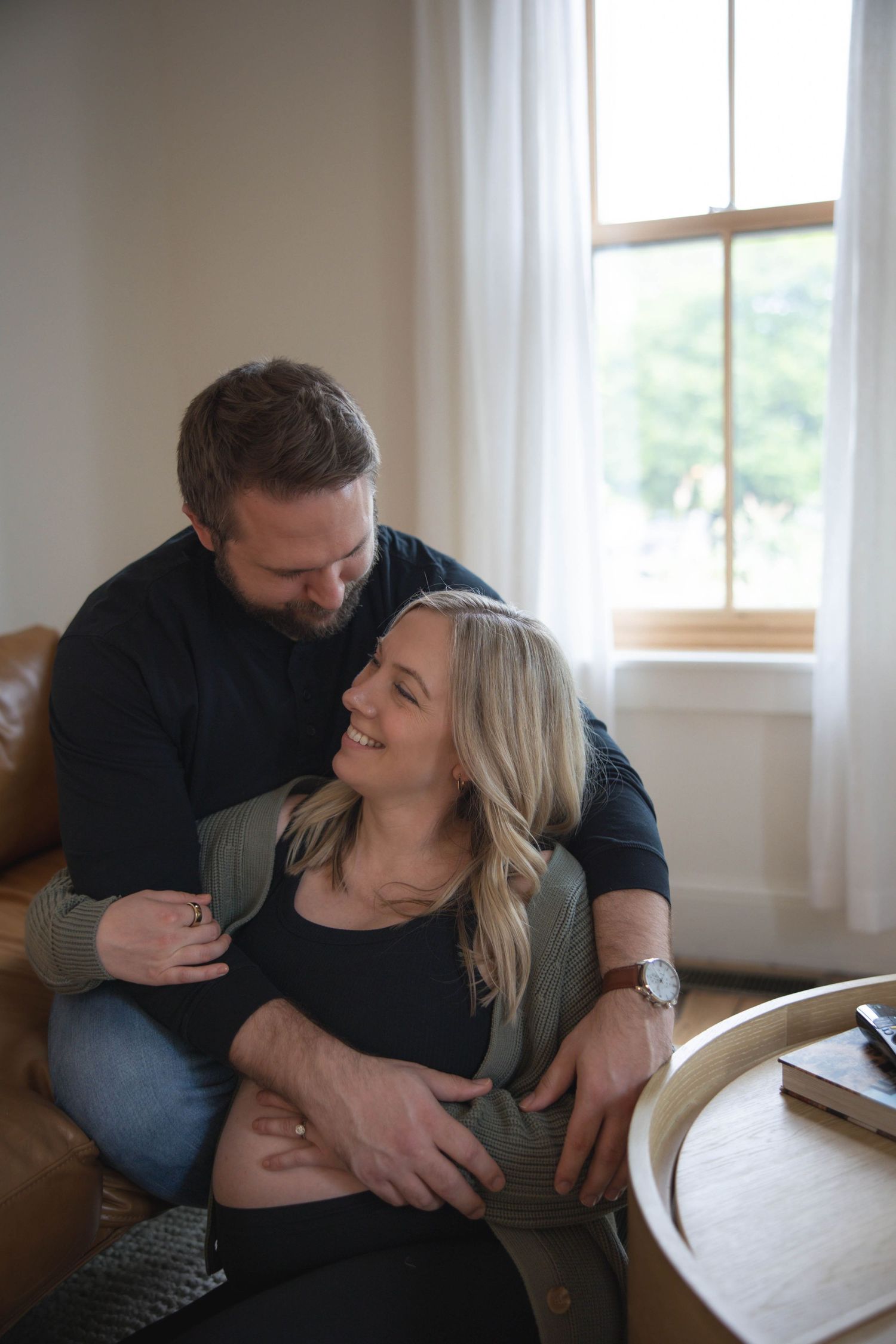 A tender moment shared on a brown leather couch in a bright, minimalist living room.