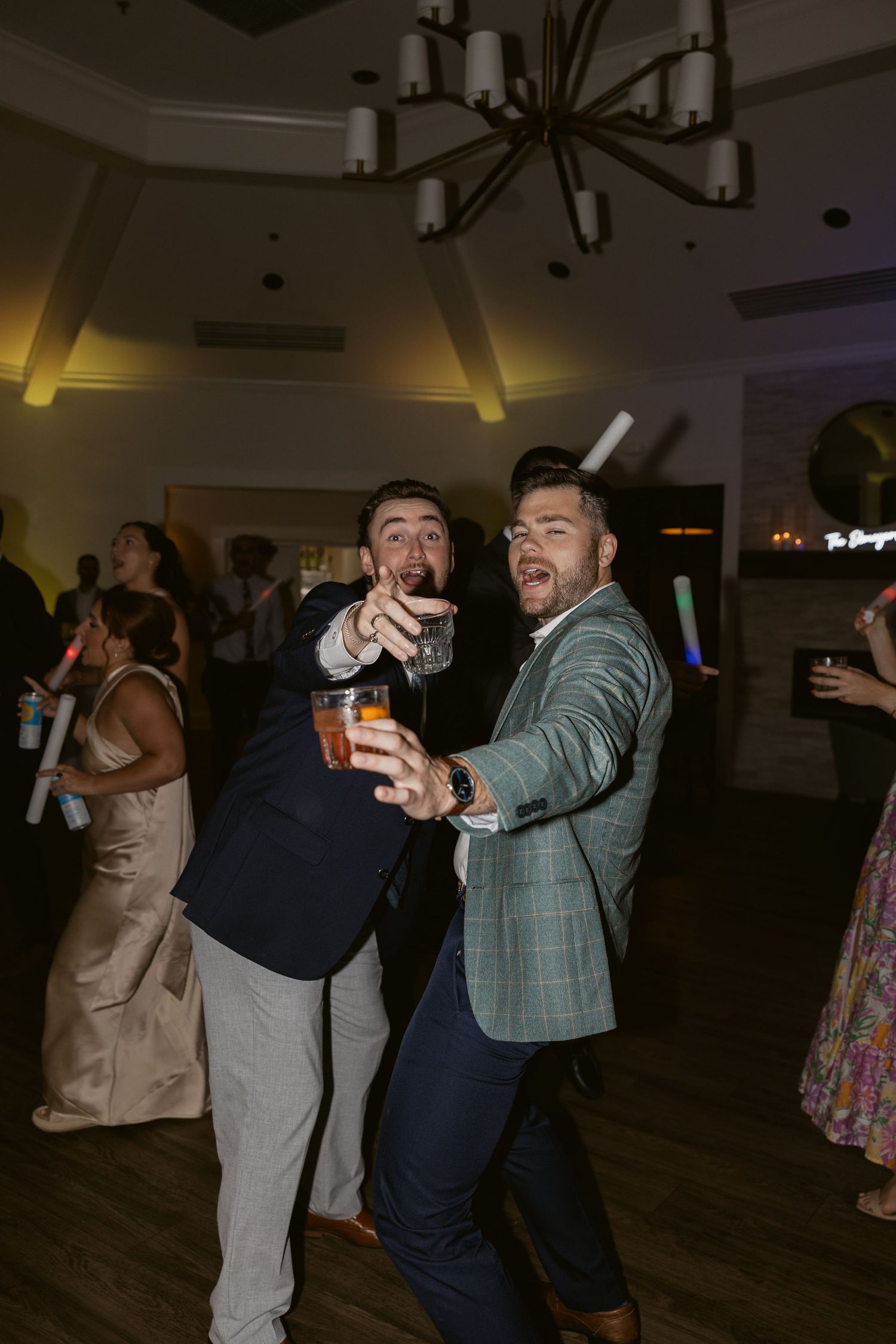 Wedding guests dancing and celebrating on dark wooden dance floor at reception.