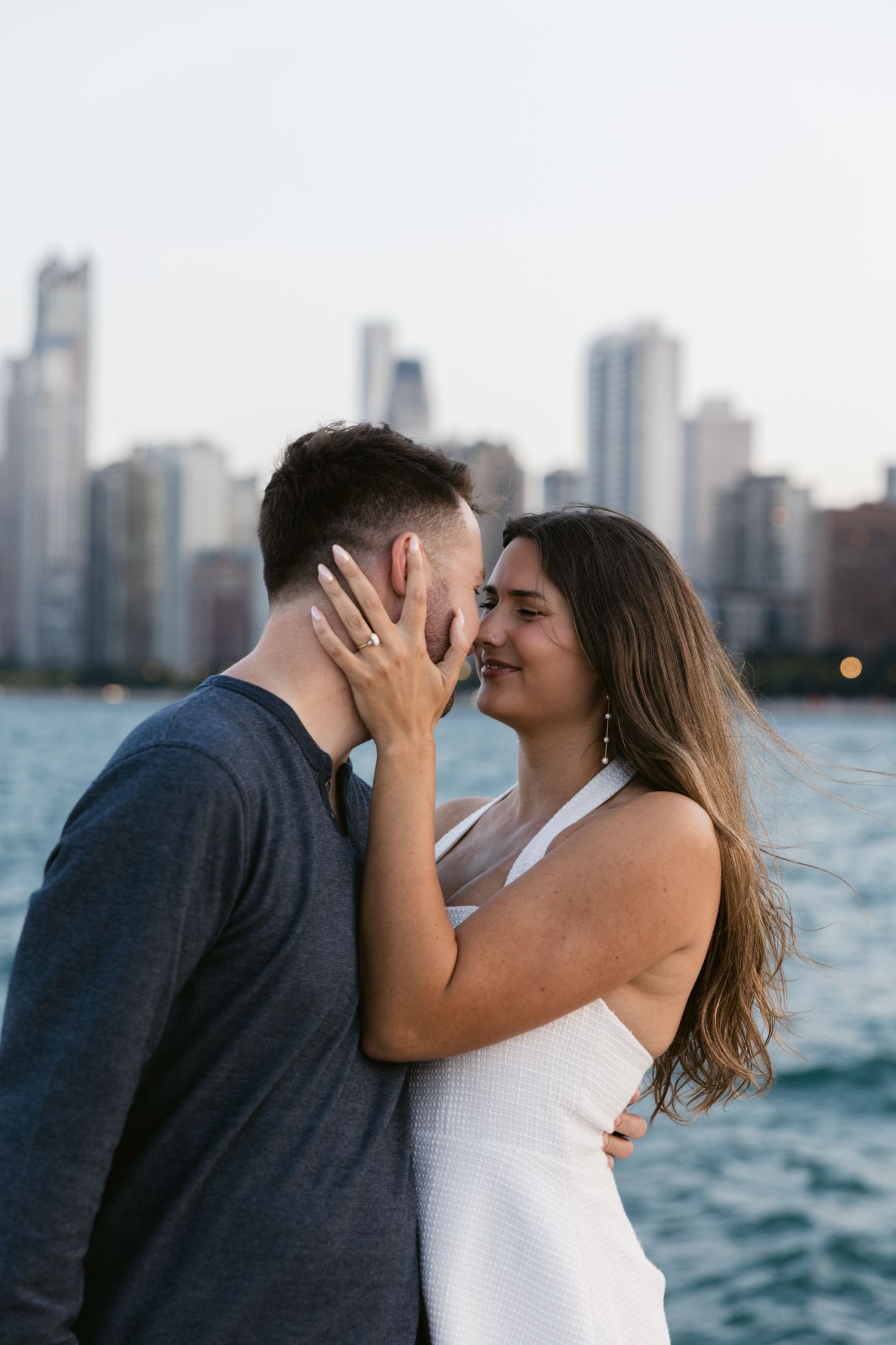 A couple sharing intimate moments against a cityscape backdrop with water and skyscrapers in the background.