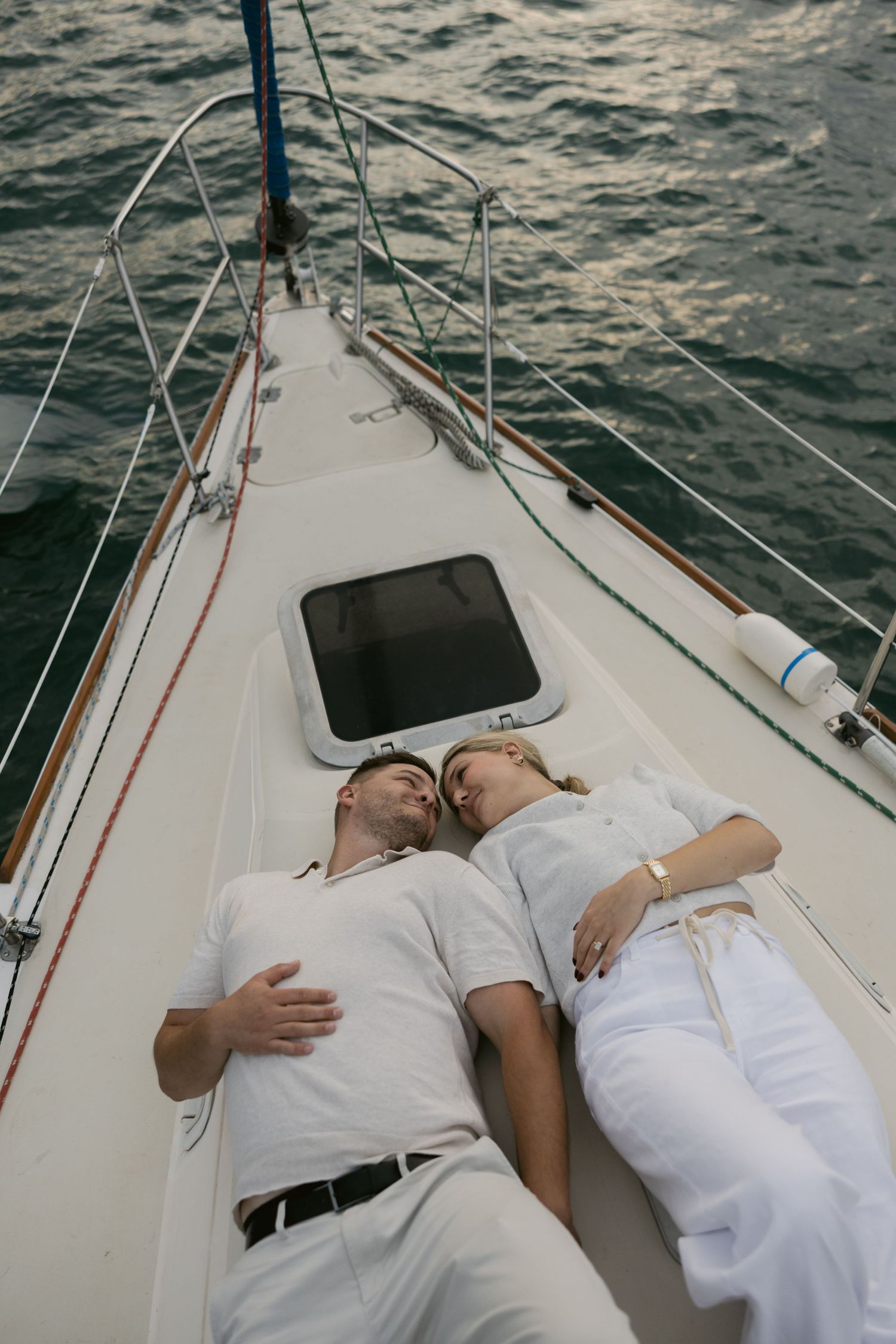 Couple relaxing together on white sailboat deck during romantic water excursion.