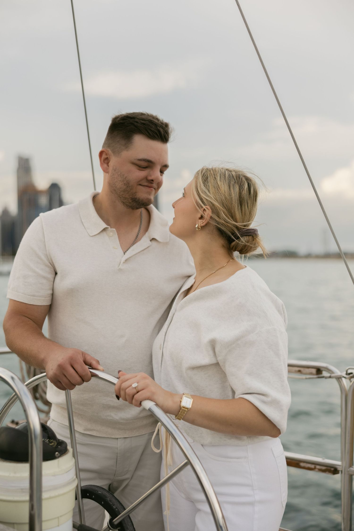 A couple shares an intimate moment while sailing, with the Detroit riverfront visible in the distance.
