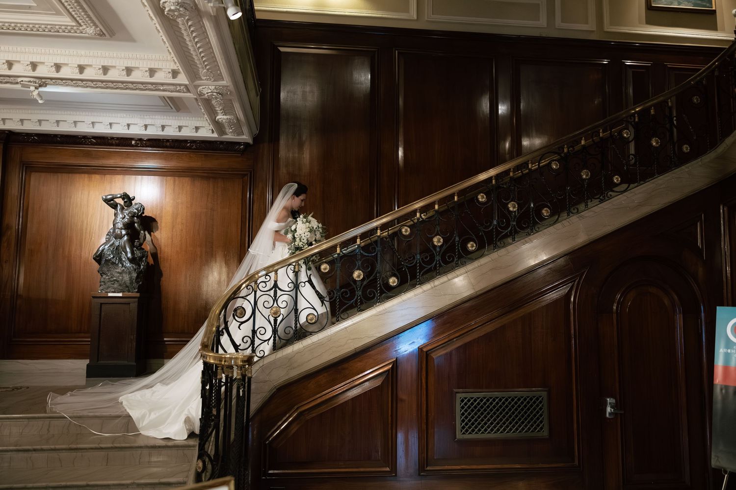 A dramatic wedding scene on a grand staircase with dark wood paneling and decorative railings.