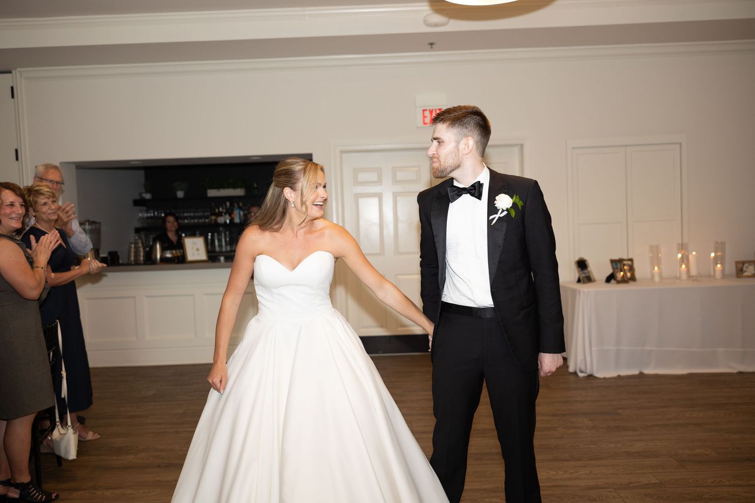 Couple dancing together in reception venue with hardwood floors and white walls.