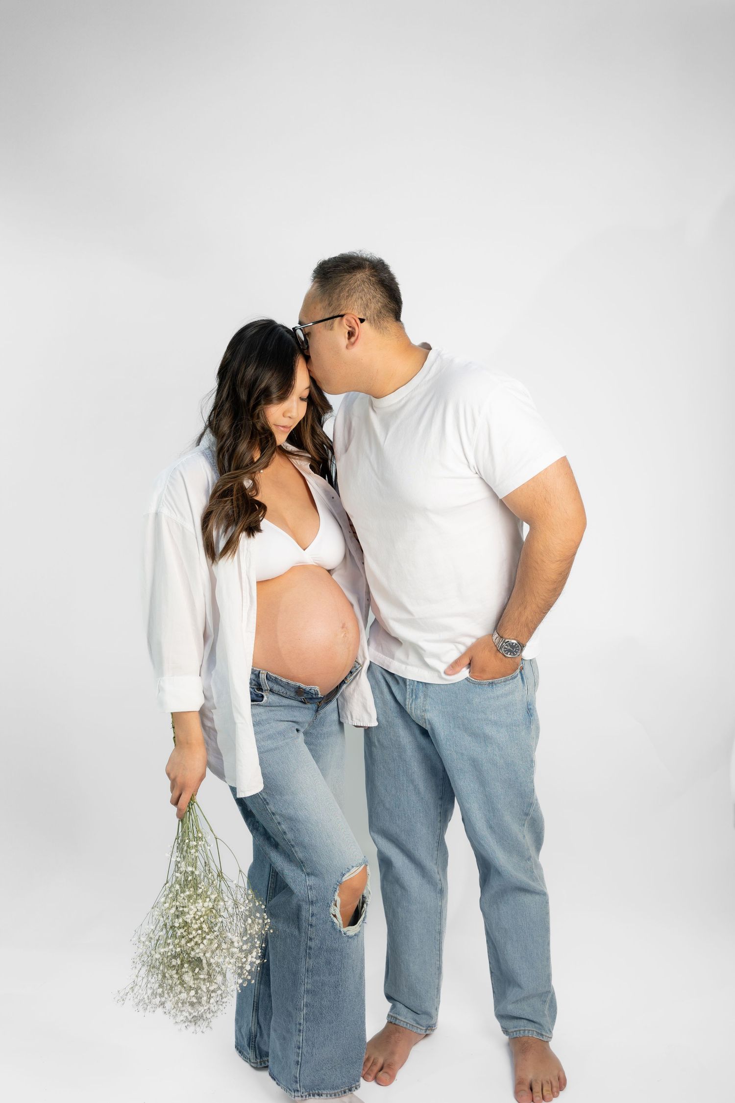 Couple in matching white and denim outfits pose romantically against grey backdrop.