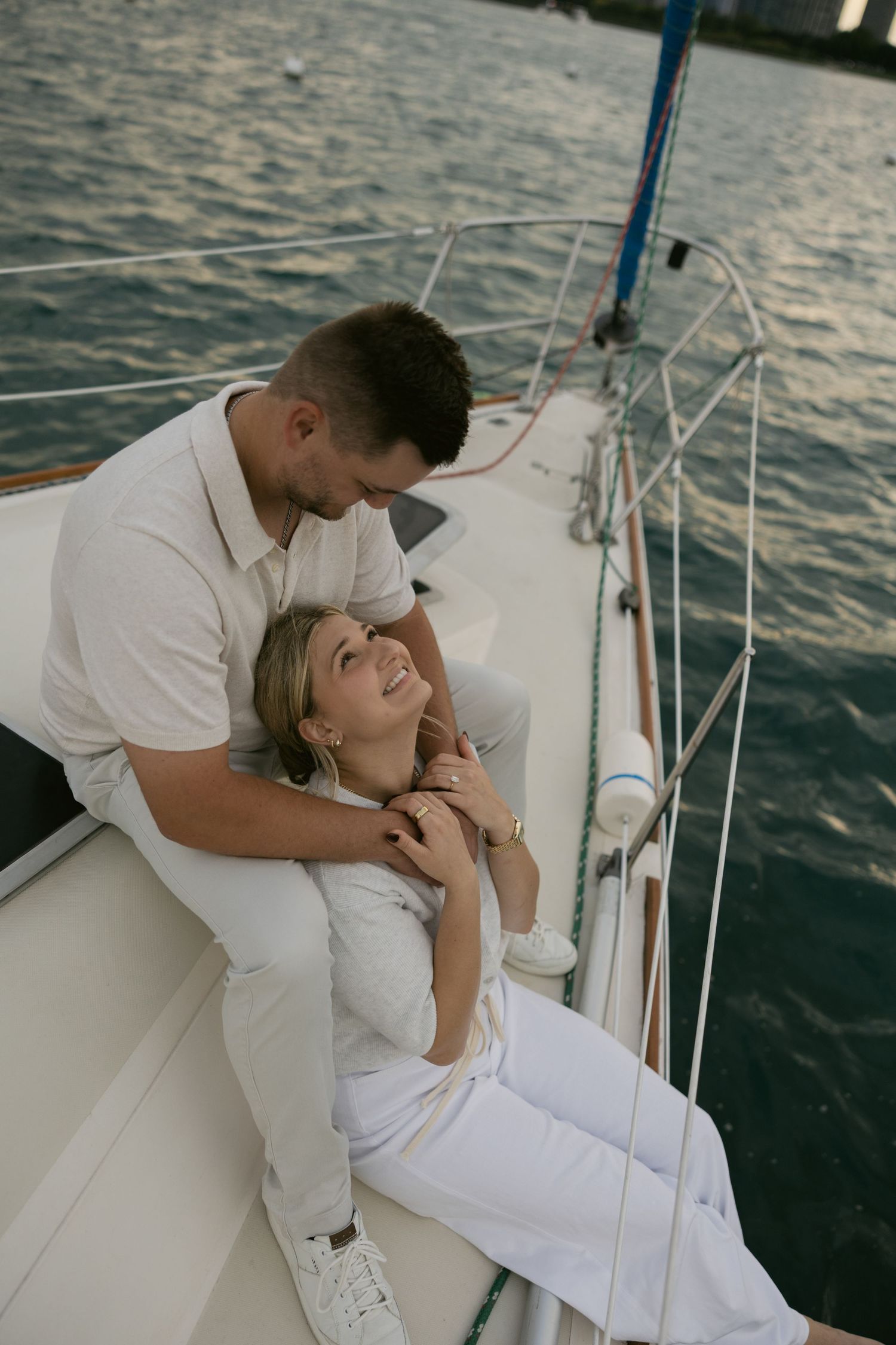 A romantic couple moment captured on a sailboat deck during sunset with the city skyline visible.