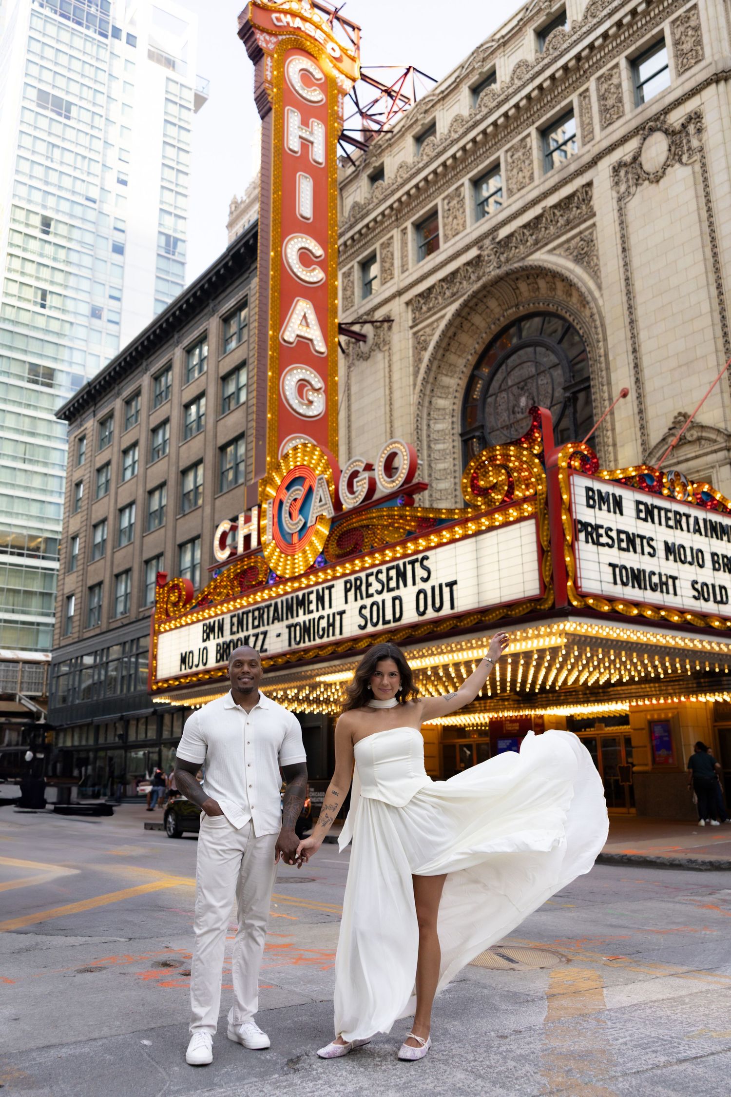 Dancing couple performs romantic poses outside illuminated Chicago Theatre.