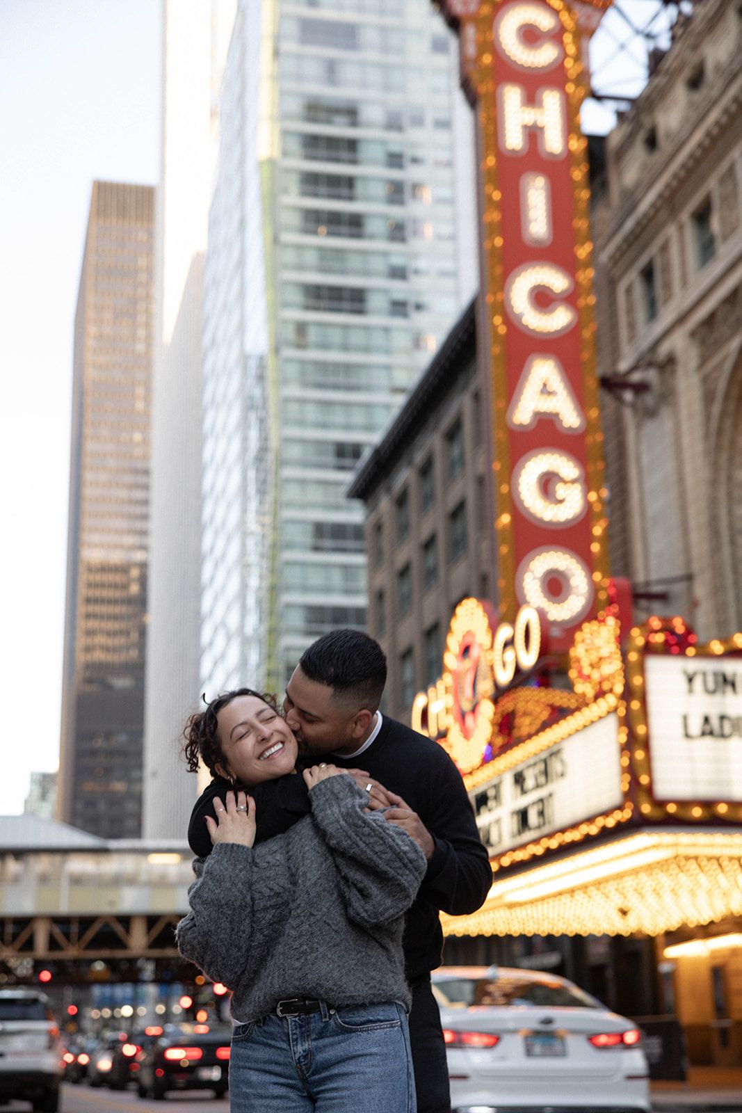 Couple embracing in front of illuminated Chicago Theatre sign at night.