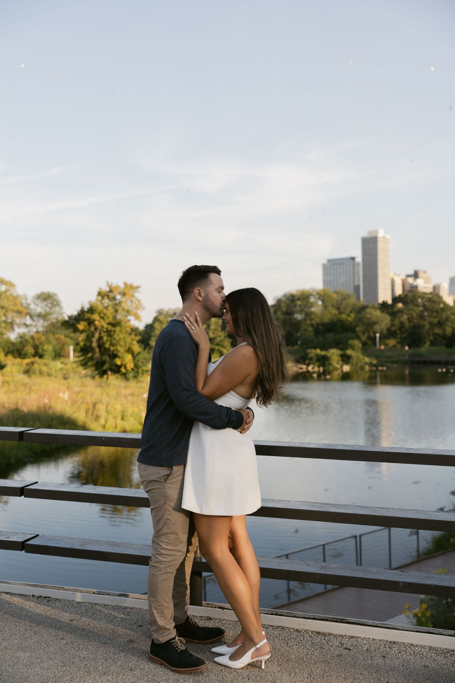 Romantic moment between couple near a city lake with skyline in background.