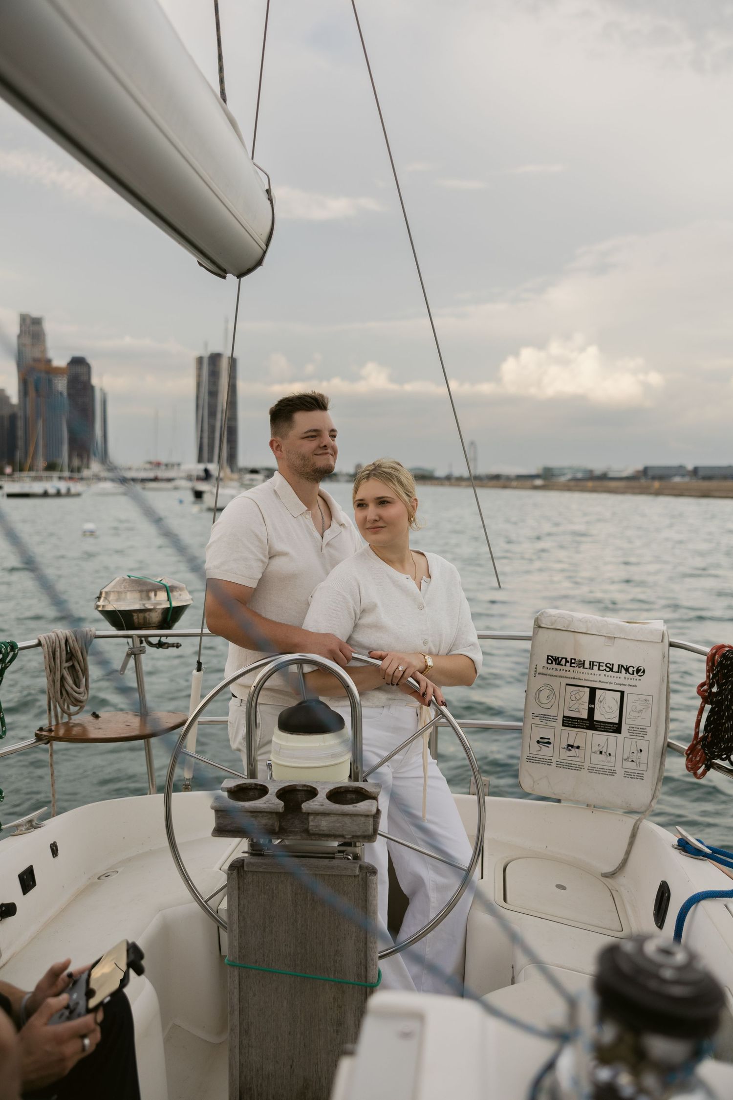 A couple in white enjoying a scenic boat ride with city skyline in the background.