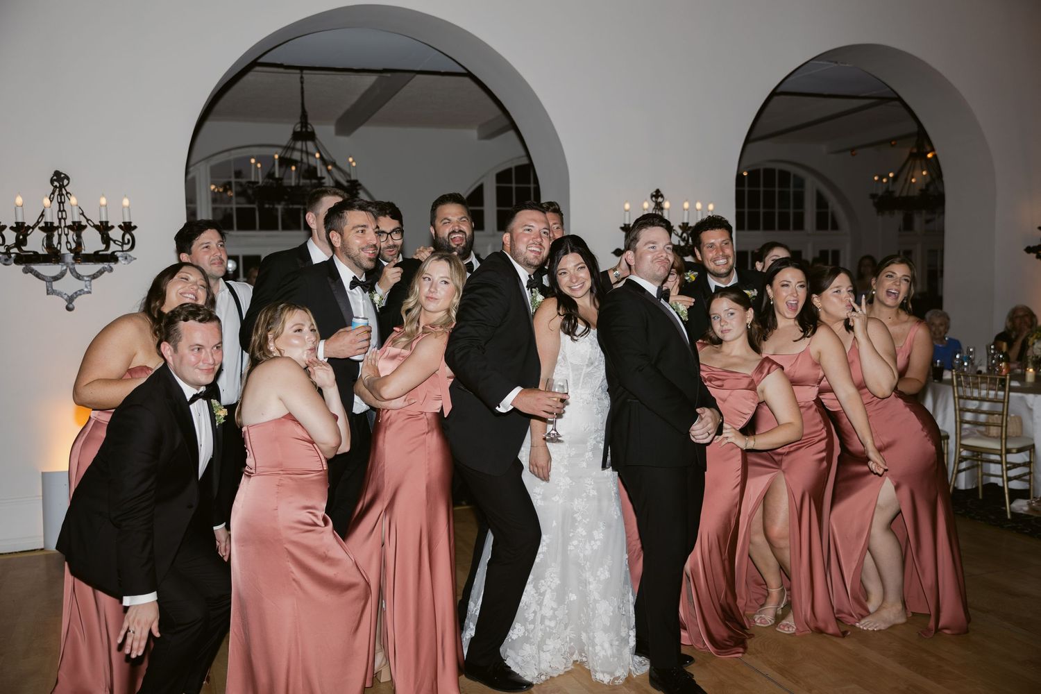 Wedding party in formal attire performs choreographed dance routine in spacious venue reception hall.