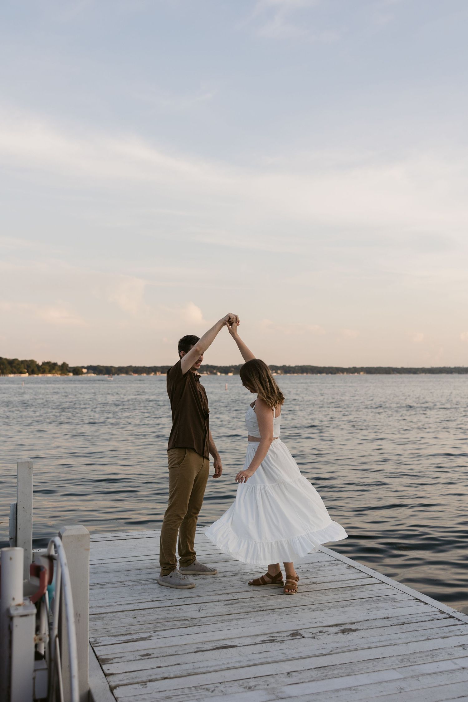A couple dances together on a wooden pier overlooking a peaceful lake at dusk.