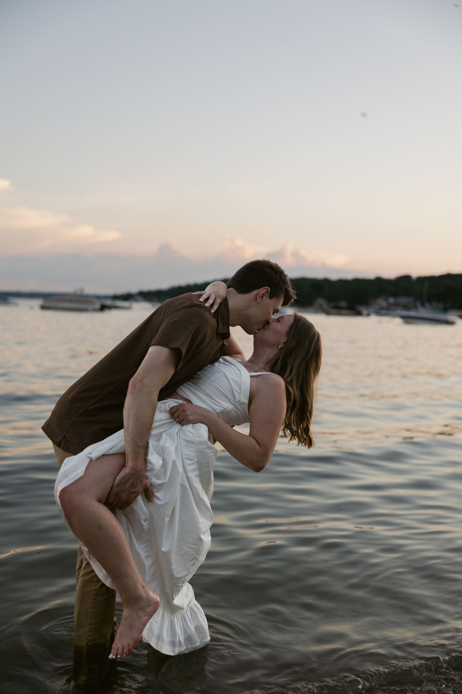 A couple performs a dramatic dance dip on a dock with the setting sun reflecting on the water.