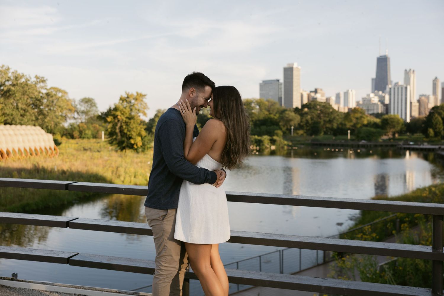 A romantic couple embraces on a rooftop terrace overlooking the Chicago skyline at sunset.