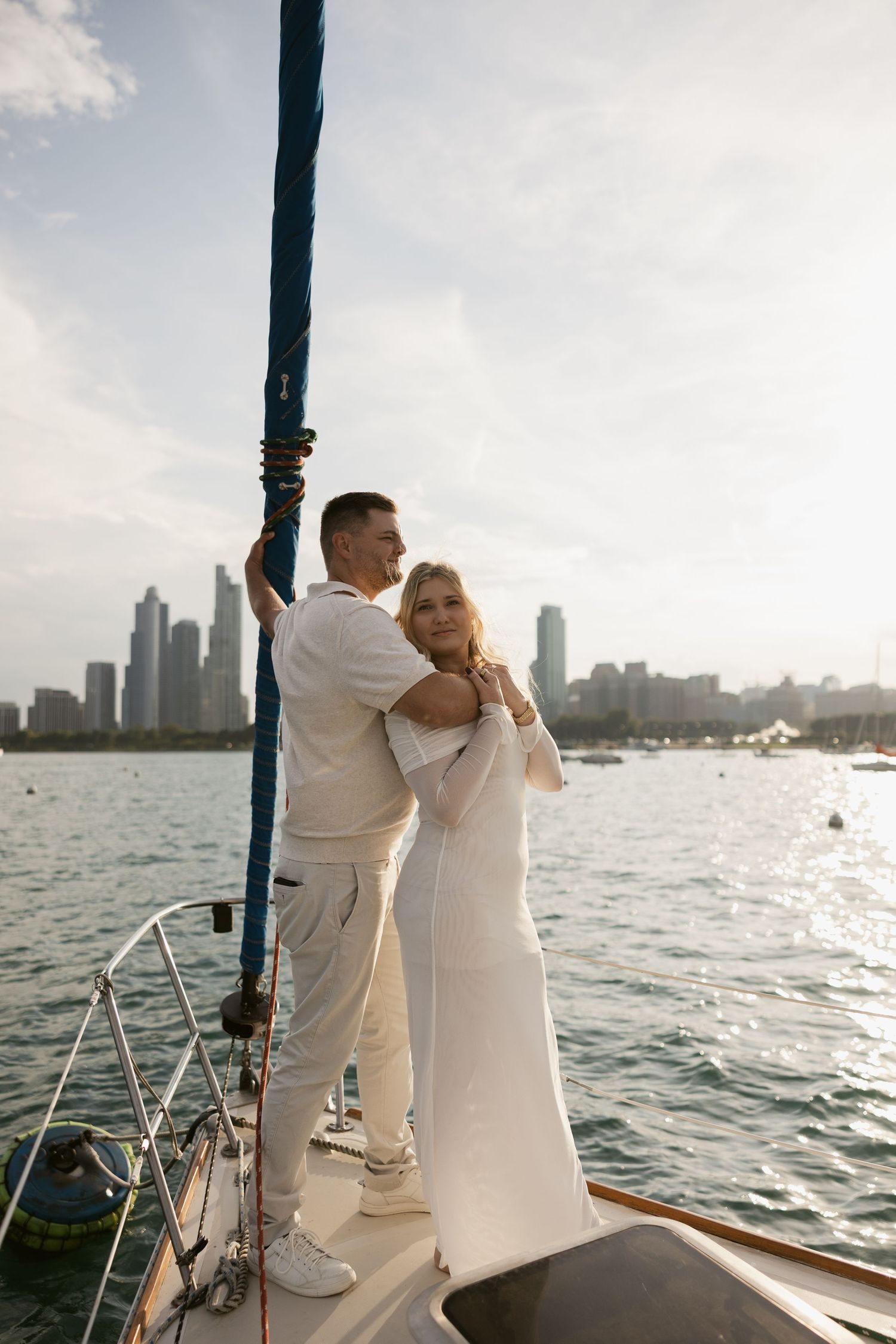Couple in white outfits sharing romantic moments on a sailboat with Chicago skyline in background.