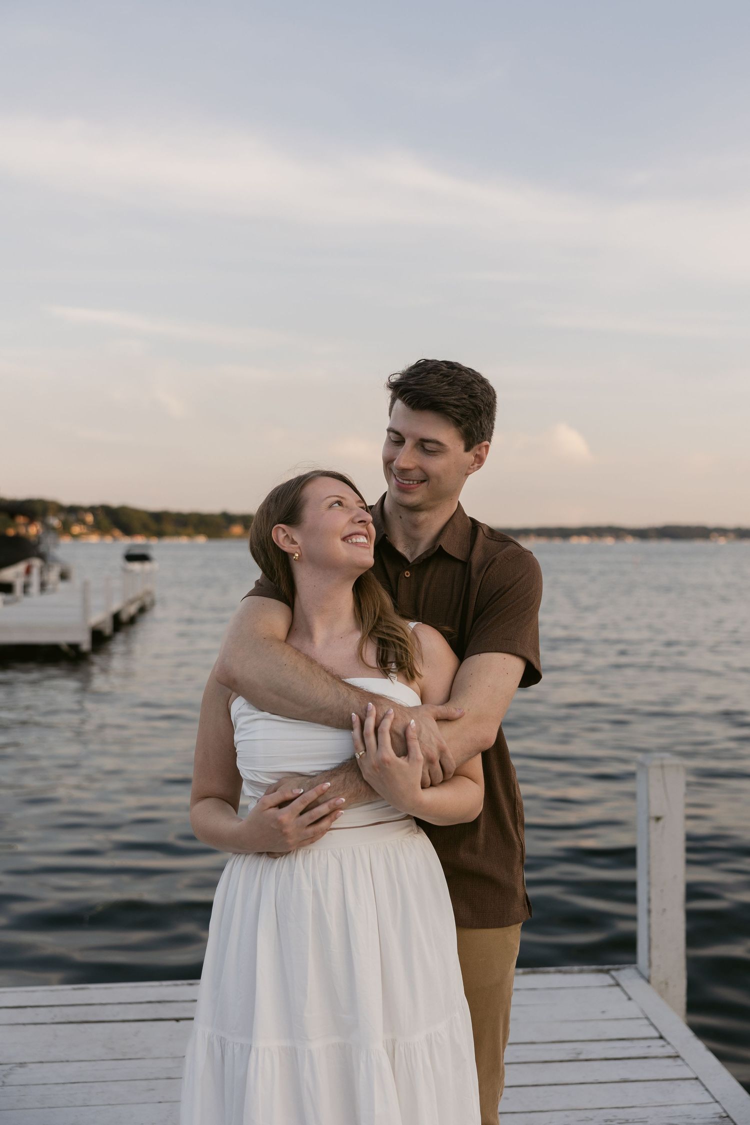 Joyful couple laughing together on dock during sunset photoshoot.