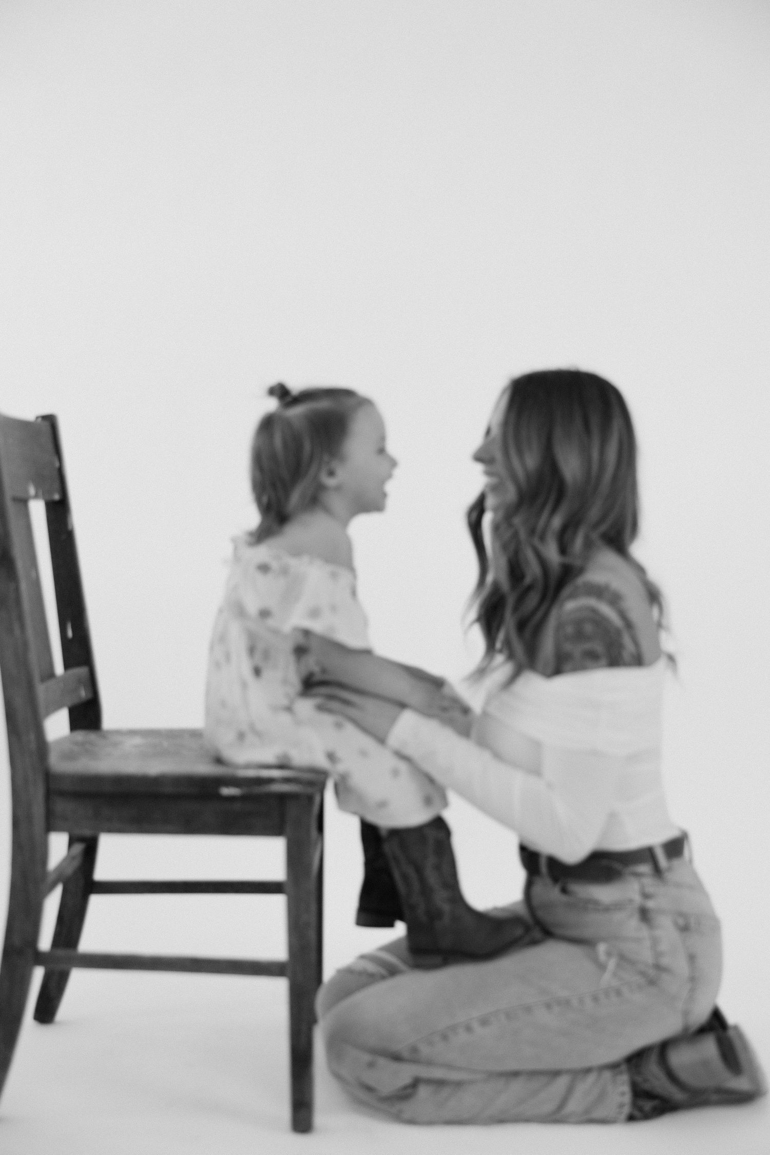 Black and white studio portrait showing playful interaction by wooden chair.