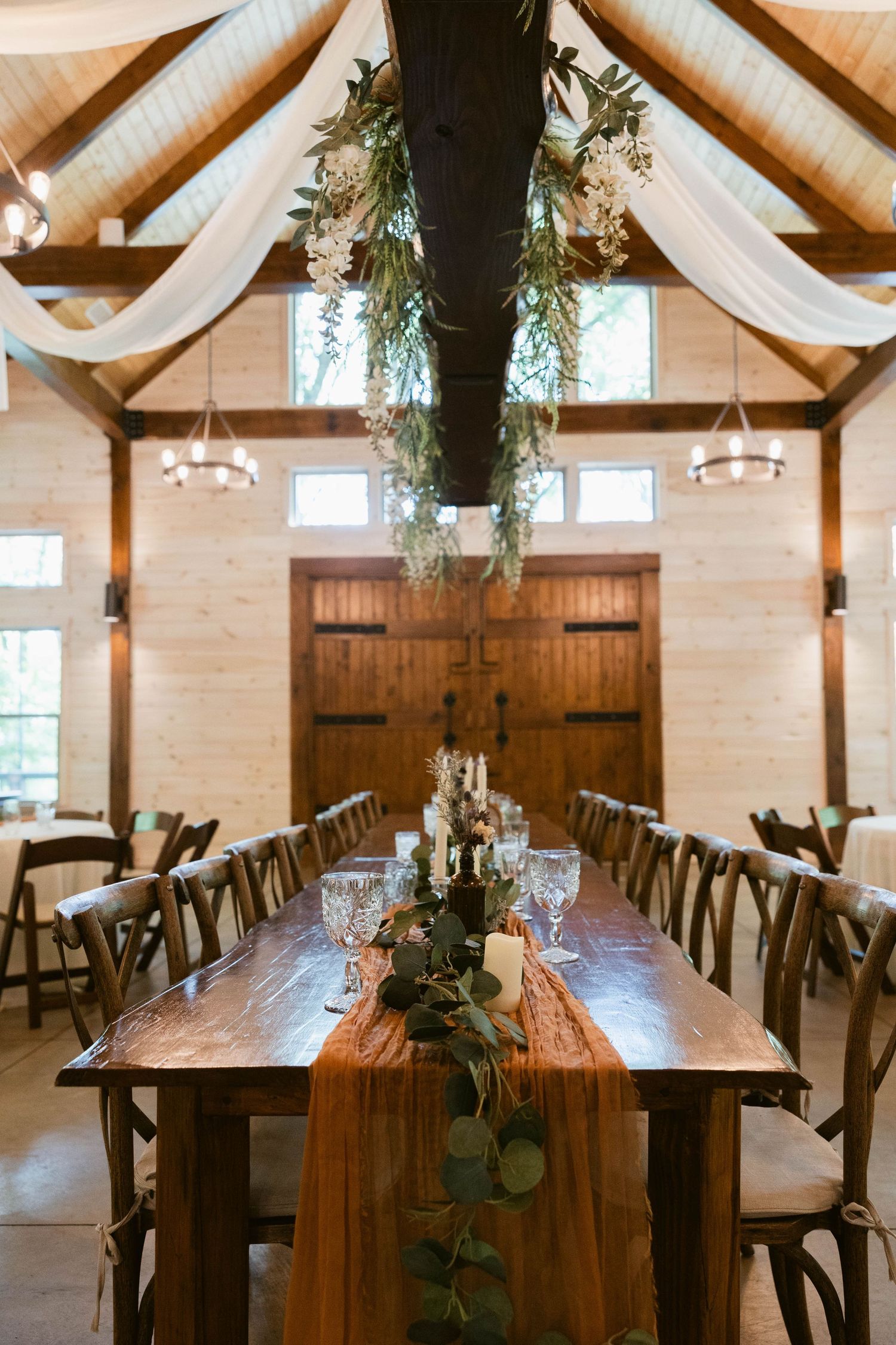 Rustic wedding reception setup with draped fabric, greenery and long wooden tables.