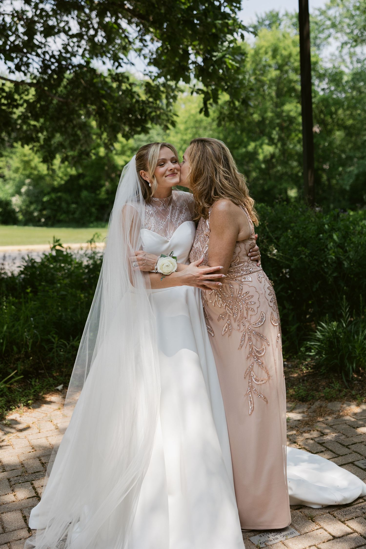 An emotional moment shared between two women in formal attire during an outdoor wedding.