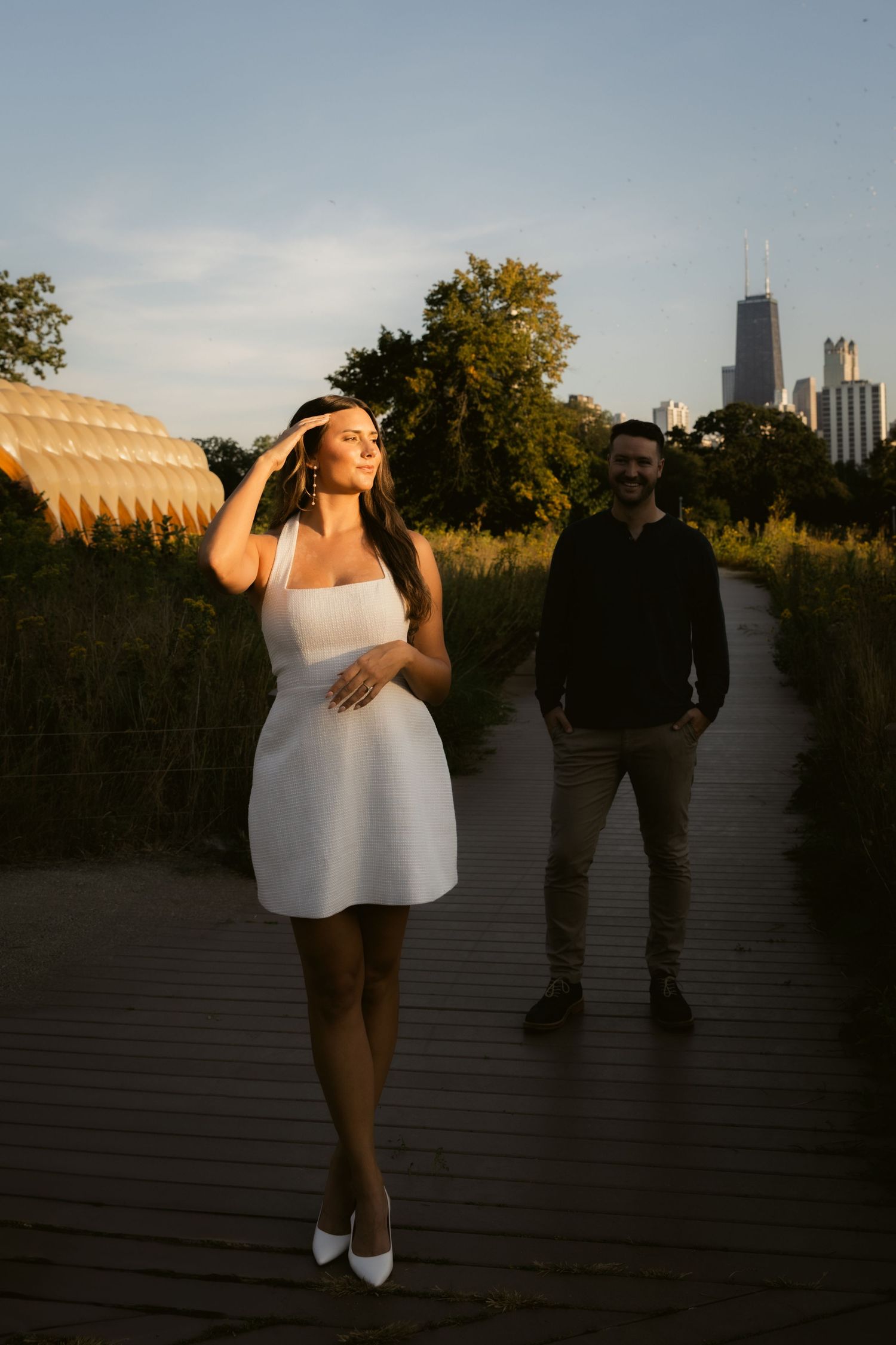 Silhouetted figures pose playfully on wooden deck with city skyline in background at sunset.