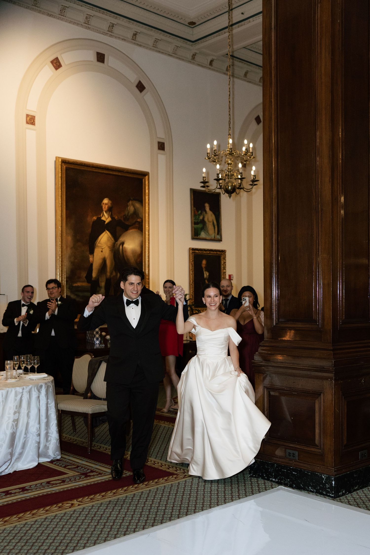 A wedding entrance into an elegant room with chandeliers and historic portraits on the walls.