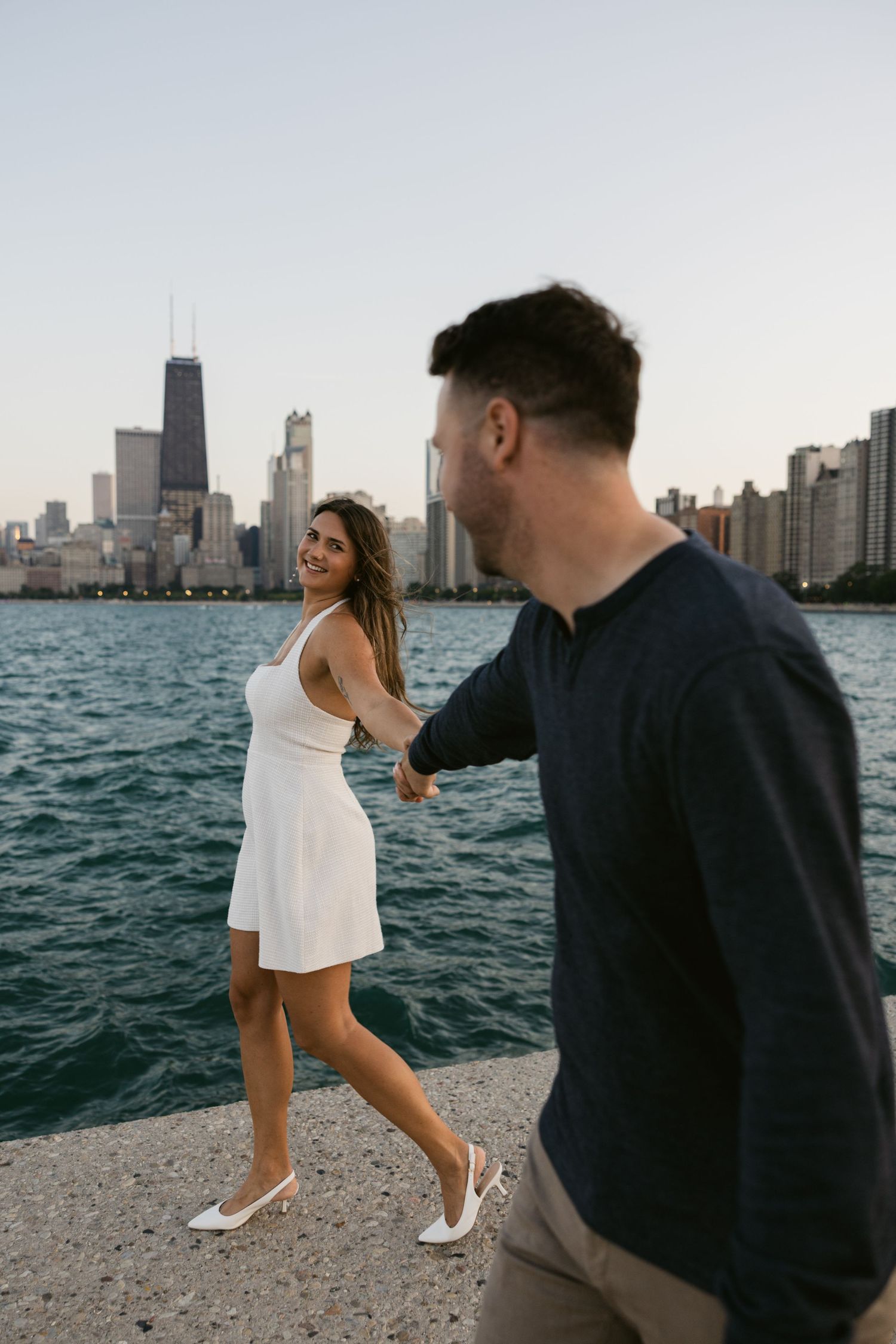 Couple enjoying playful moments along Lake Michigan's shore with Chicago skyline in view.