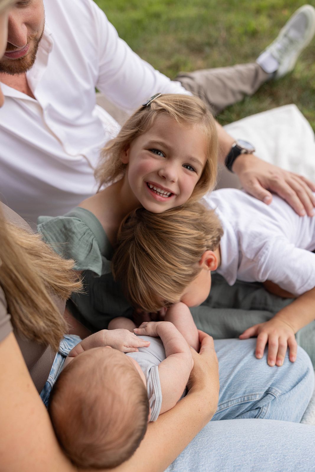 Family lying on grass together during outdoor photo session with infant.