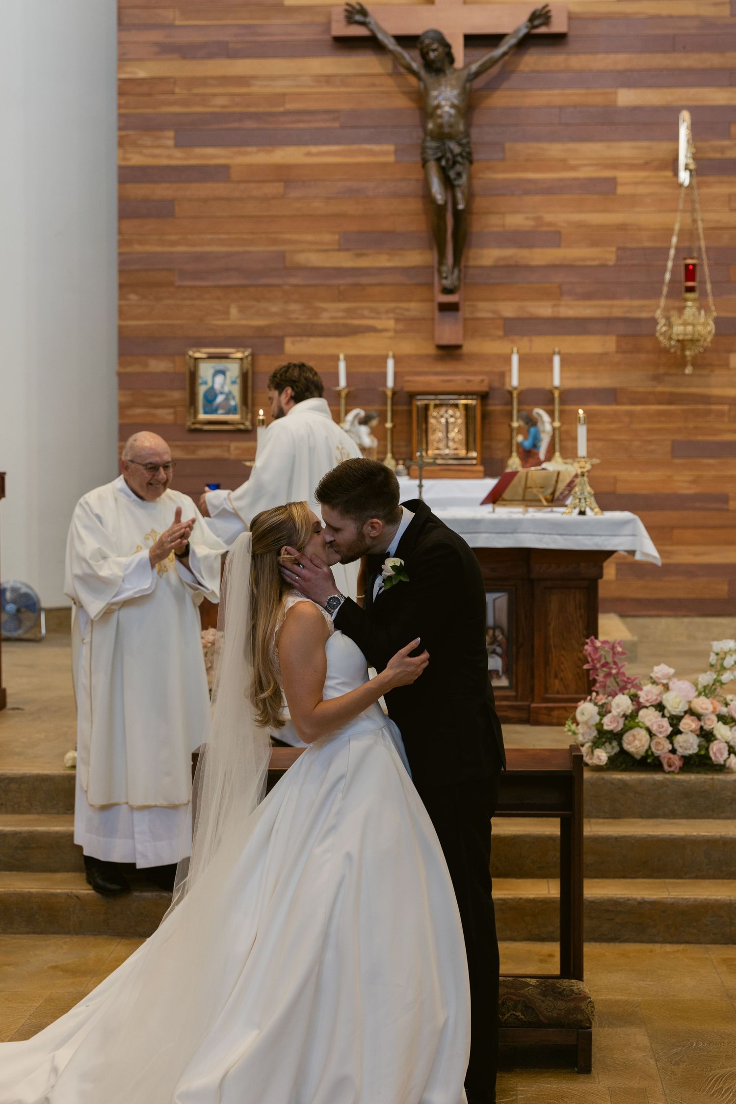 Traditional Catholic wedding ceremony taking place in a modern church with wooden walls and crucifix.