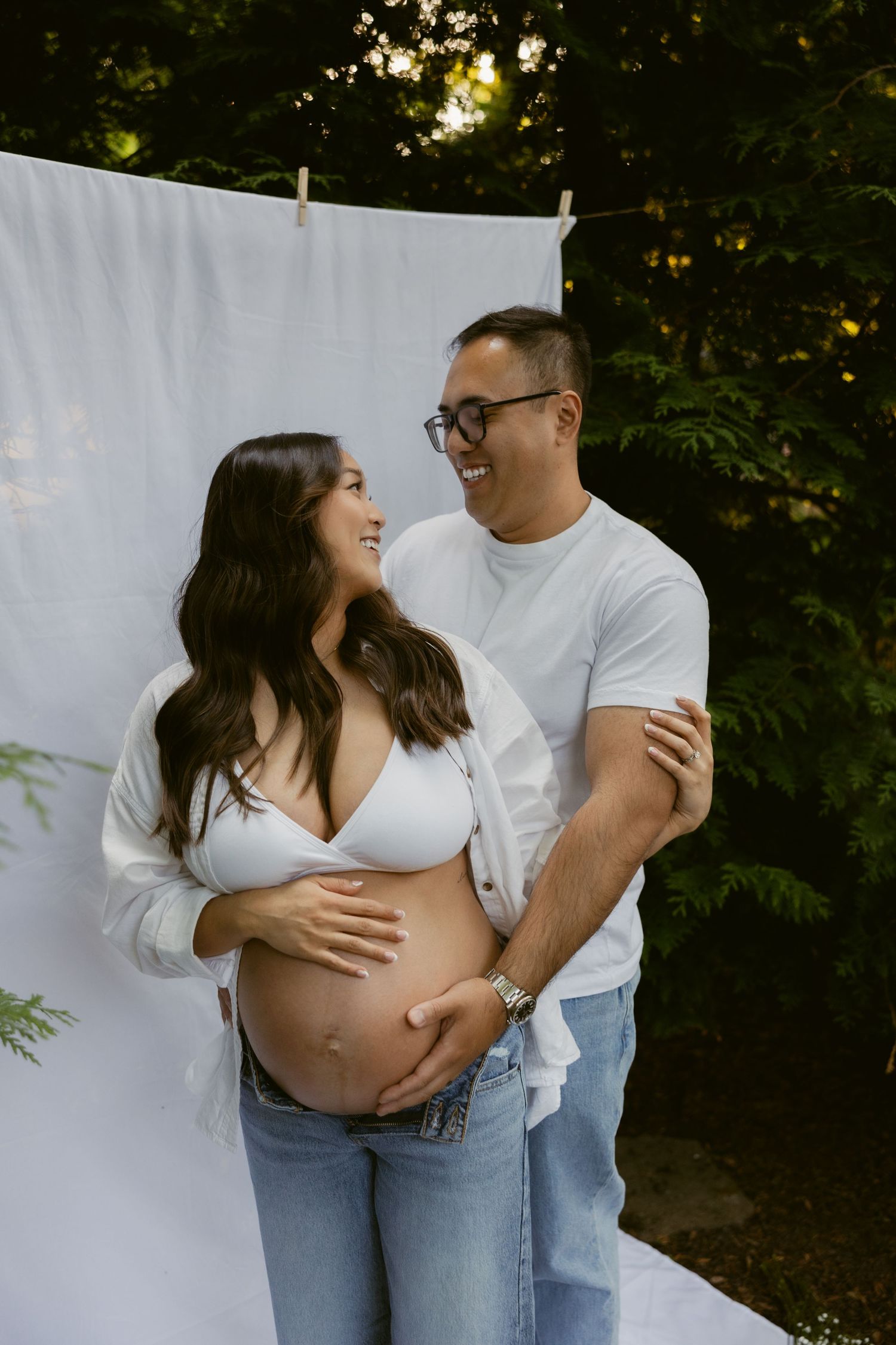 A joyful maternity photography session showcasing an expecting couple in casual denim and white outfits.