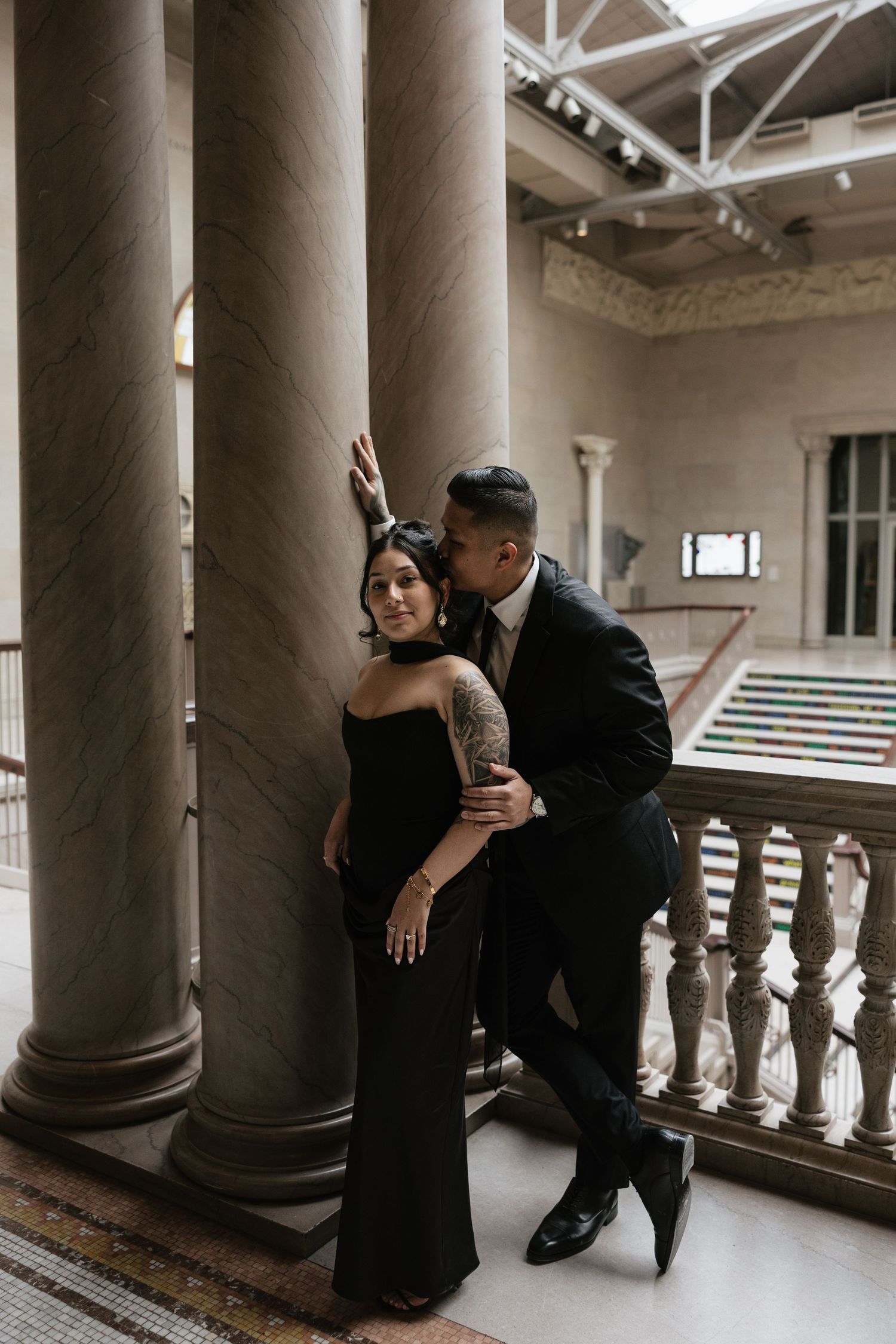 Elegant couple posing between classical columns in historic building interior.