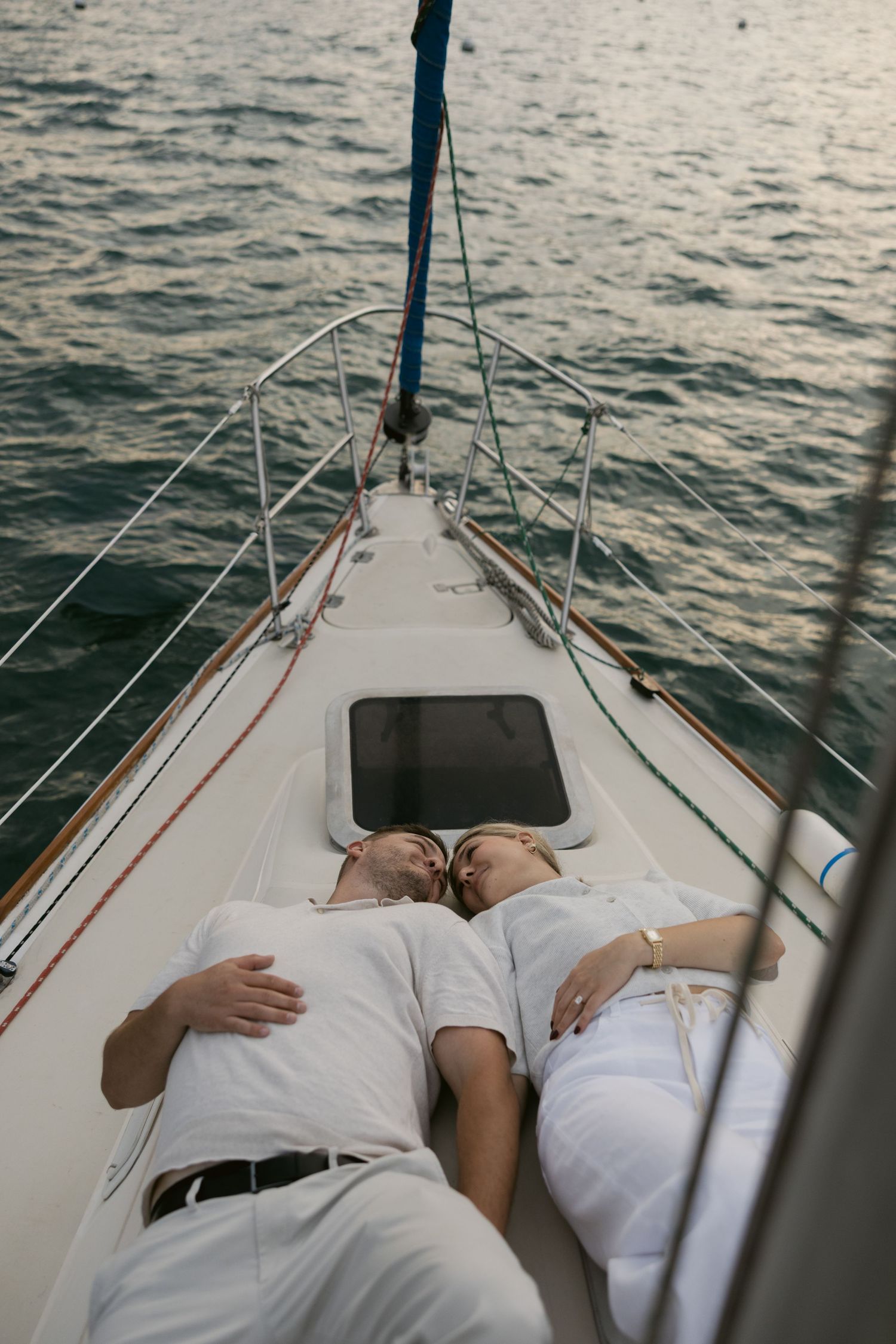 Couple lying peacefully on white boat deck during sunset sail.