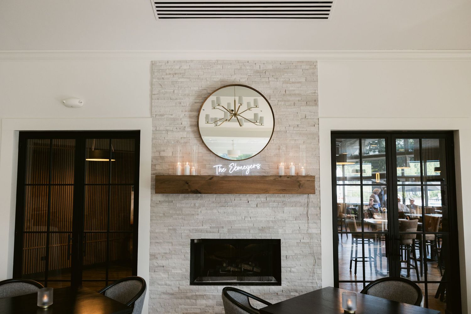 Modern white brick fireplace with round clock and dark glass doors in elegant interior.